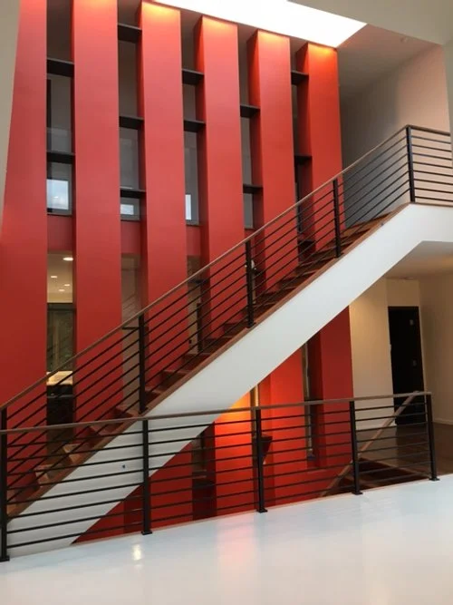 Modern interior with a staircase featuring black railing and wooden steps, set against a red accent wall with vertical panels.