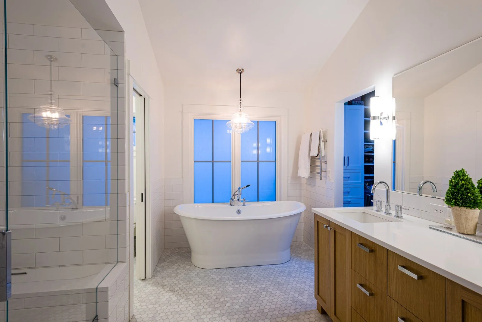 Modern bathroom with a free-standing bathtub, a glass-enclosed shower, a double sink vanity with a wood cabinet, white subway tiles, and a large window with frosted glass.