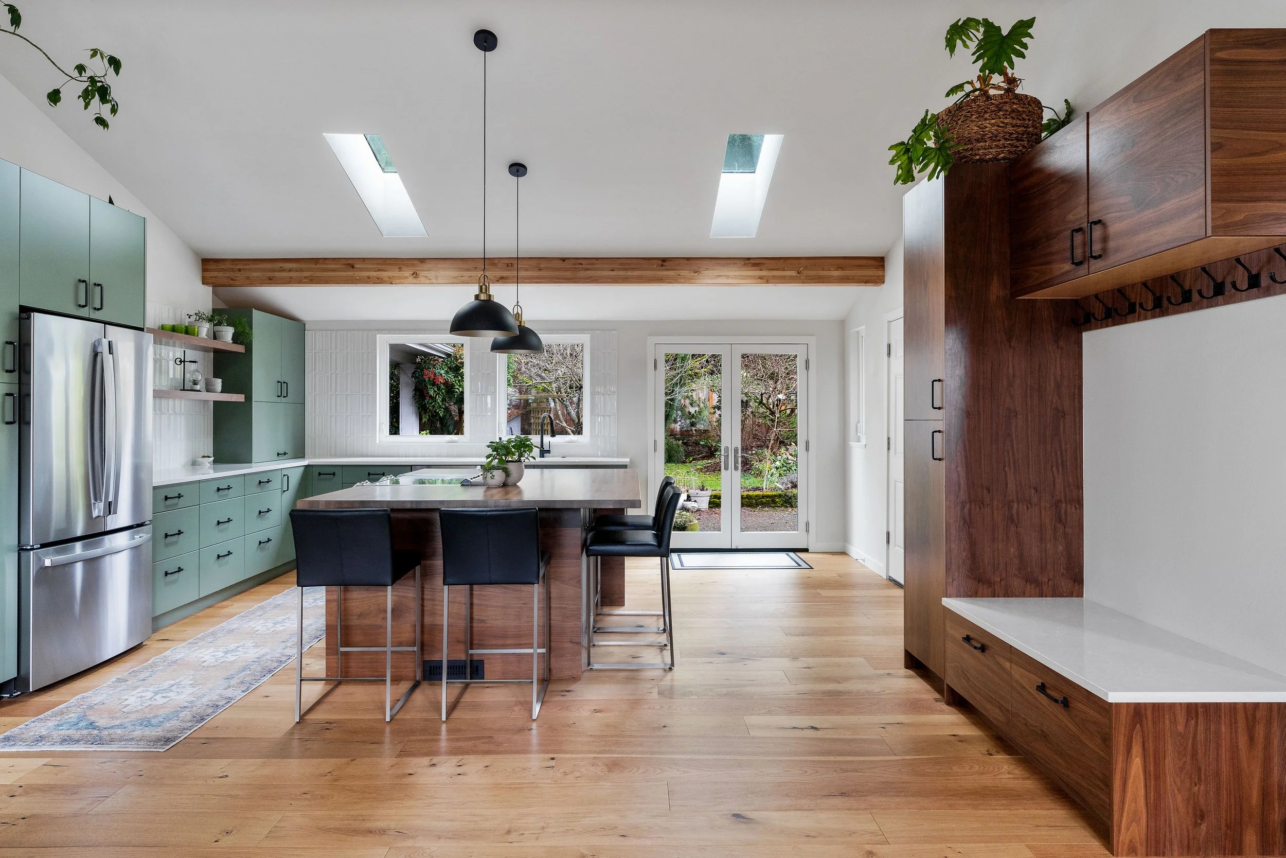 Modern kitchen with green cabinets, wooden island, black pendant lights, and large windows overlooking a garden
