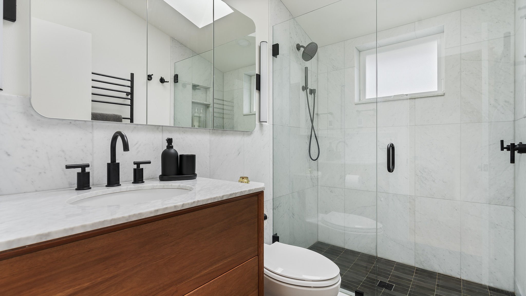 Modern bathroom with a vanity, black fixtures, a glass-enclosed shower, and a small window.