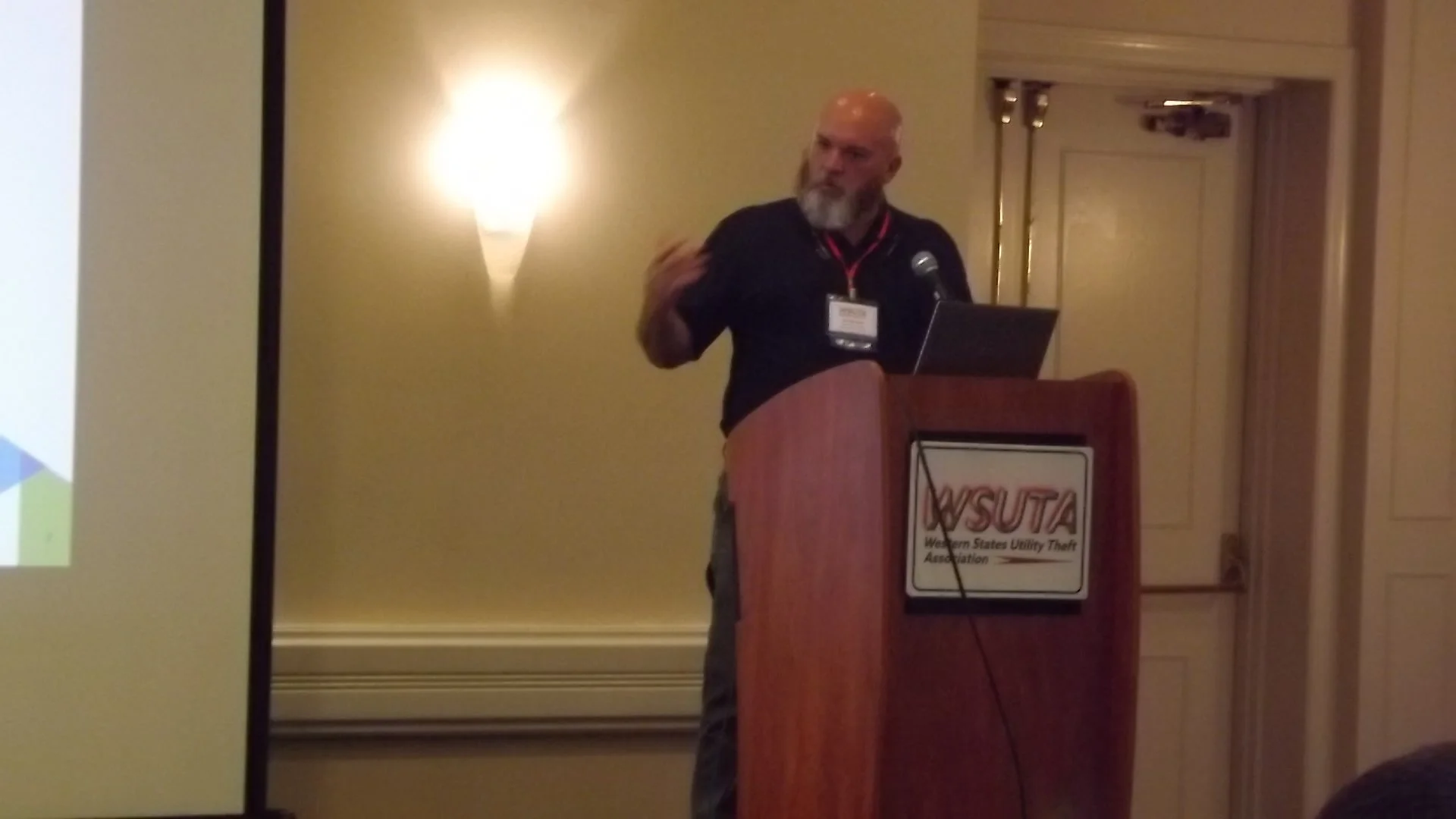 A man with a shaved head and gray beard giving a presentation at a podium with a sign that reads WSUTA.