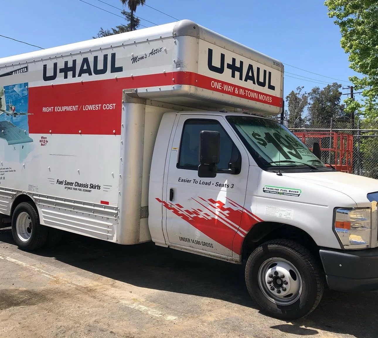 U-Haul moving truck with red and white branding, parked on a street, advertising one-way and in-town moves, fuel saver features, and a price of $129 for rental.