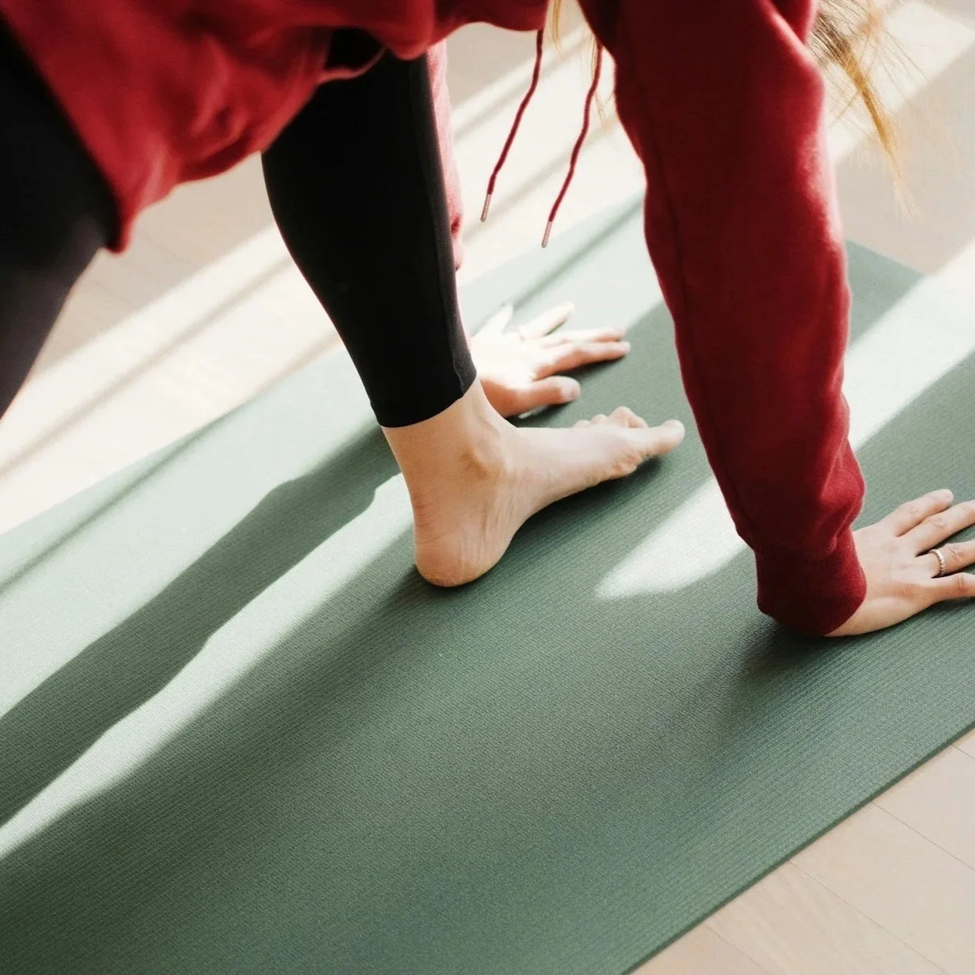 Person practicing yoga in downward dog pose on a green yoga mat, wearing black leggings and a red long sleeve shirt.