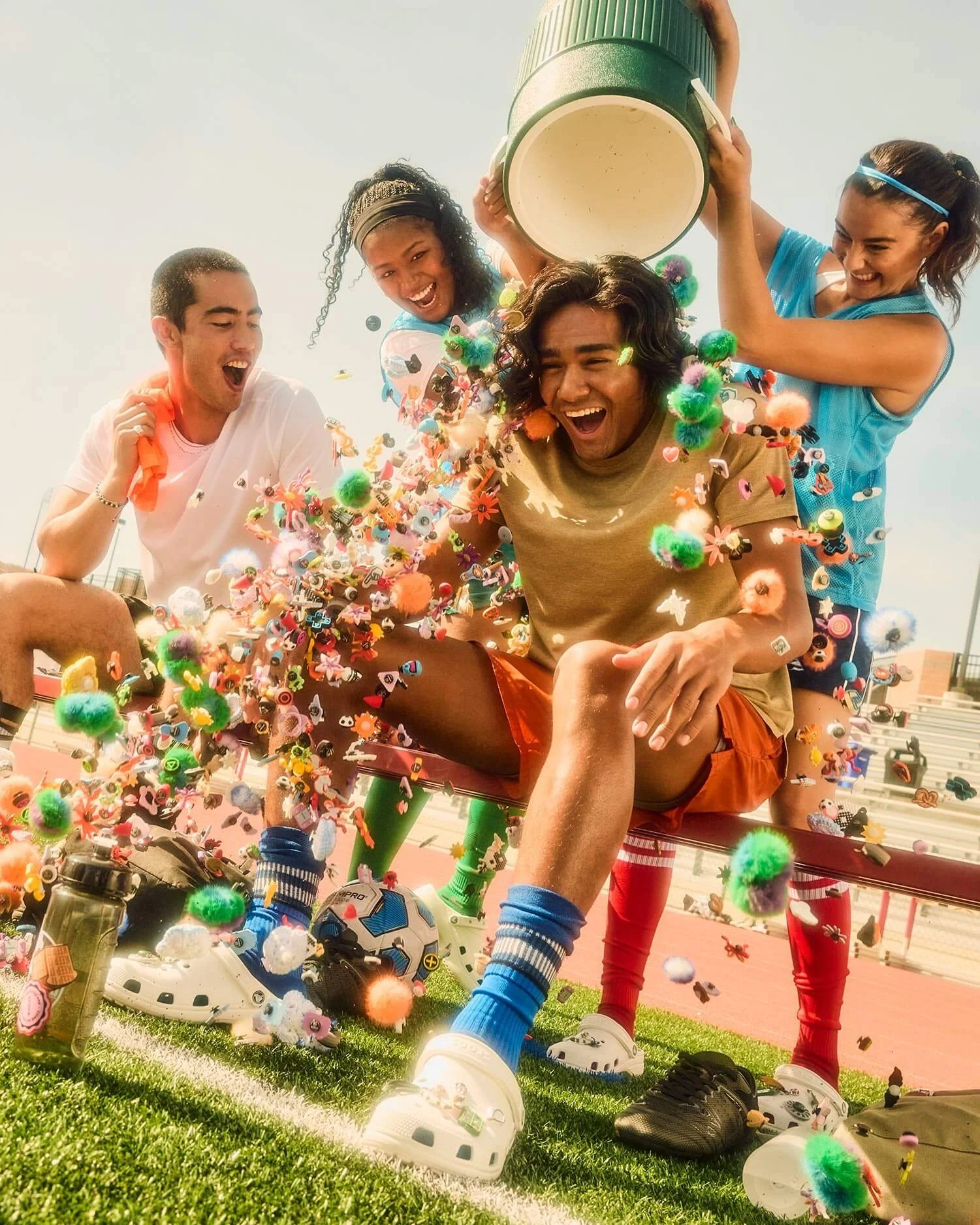 Group of young people celebrating with confetti on a sports field, cheering and smiling wearing Crocs.