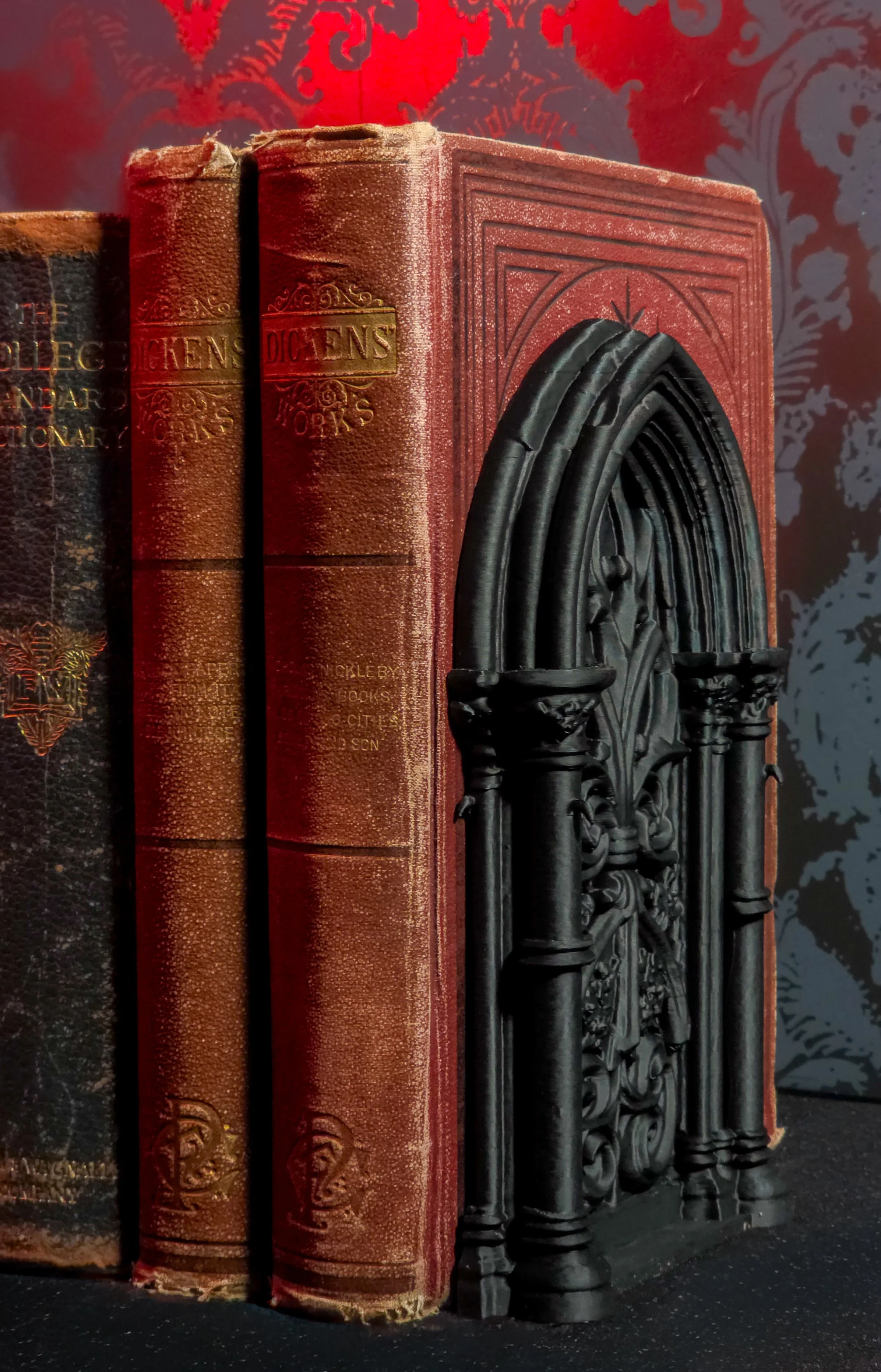 Close-up of three old, worn books, with a decorative, black Gothic-style bookend resembling a church Gothic window, against a dark red and gray textured background.