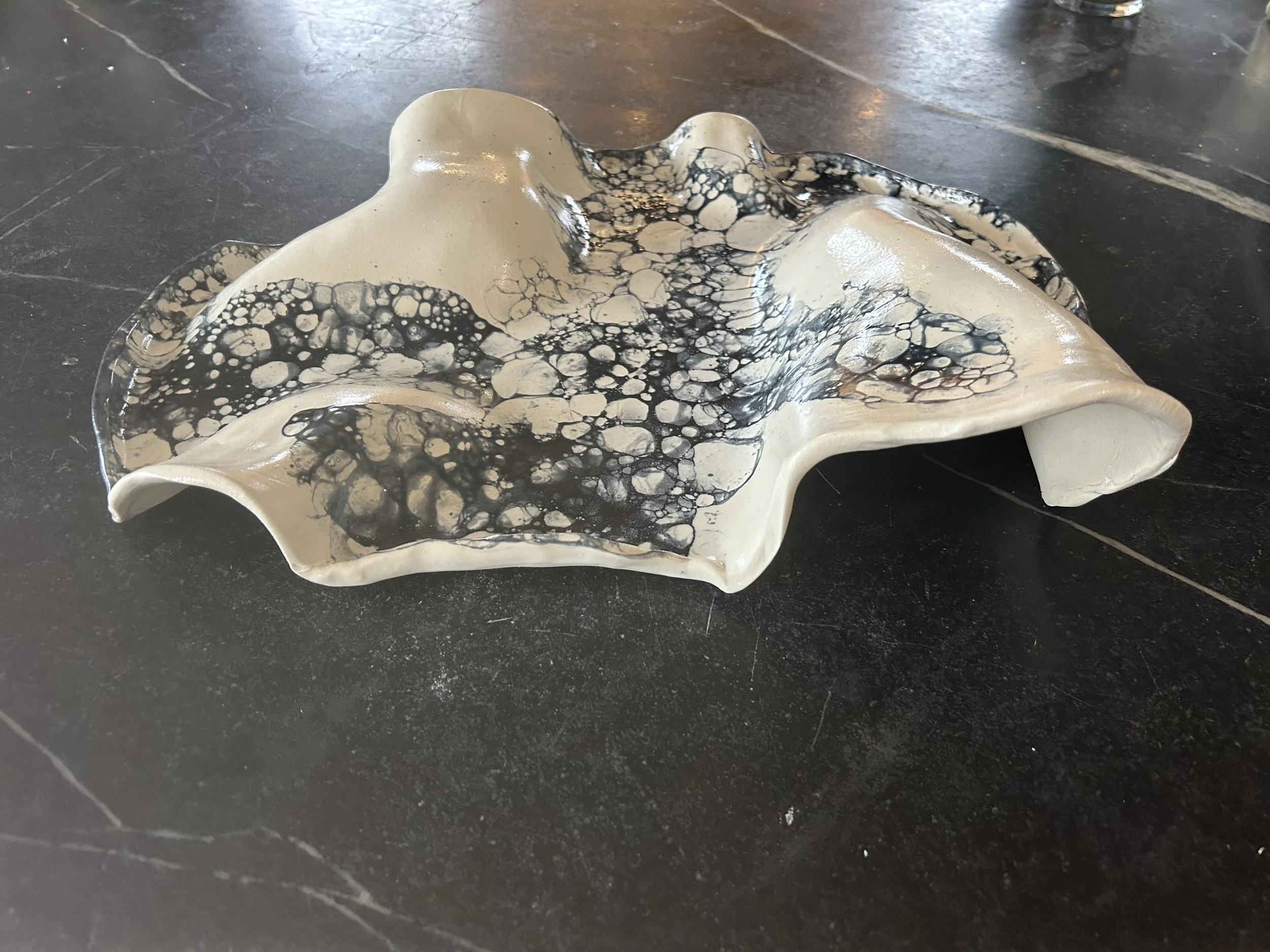 A ceramic sculpture with irregular edges and a bubbly, textured surface, featuring a pattern of black and white bubbles.