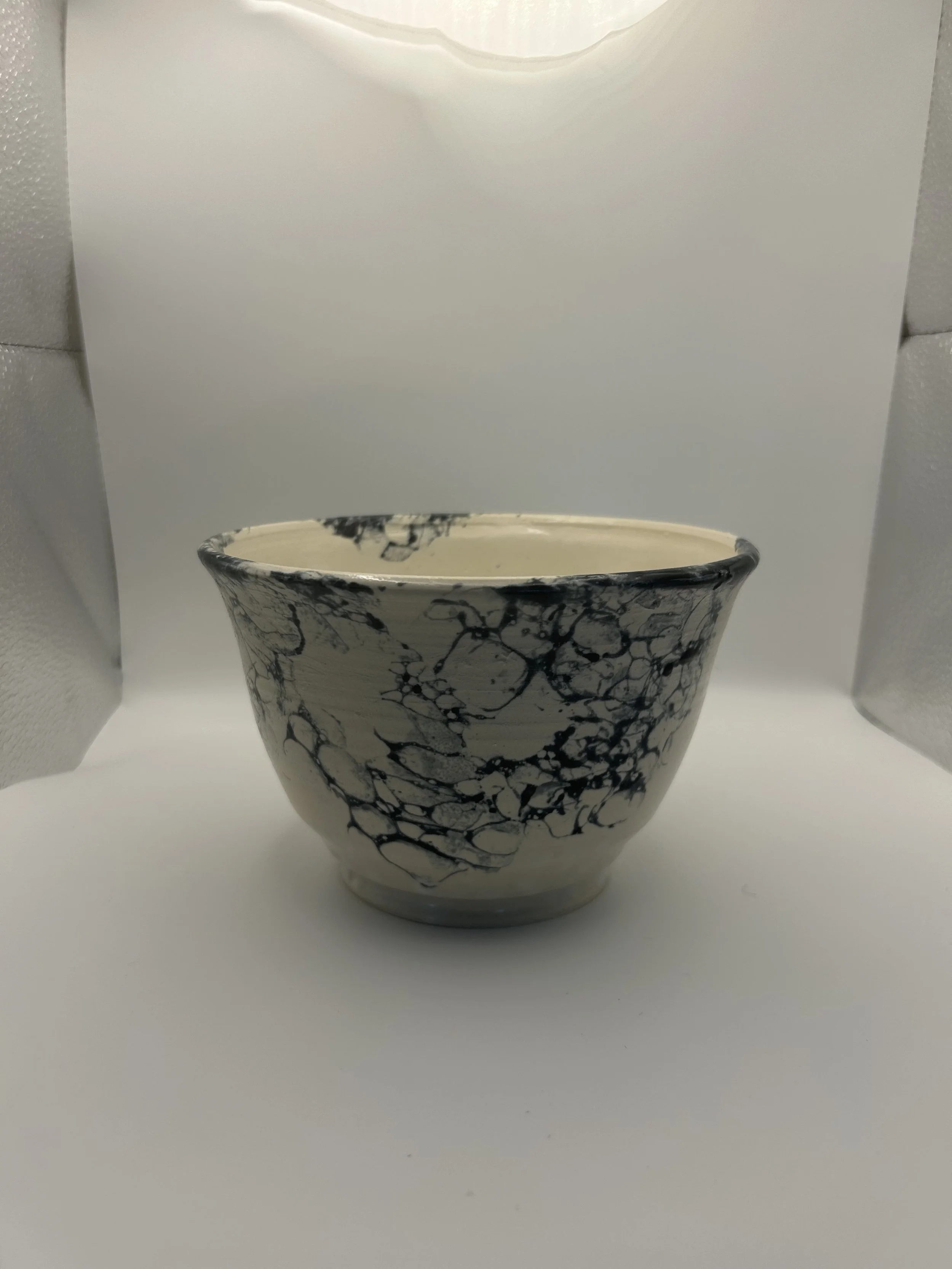 A white ceramic bowl with black marble-like veining, placed on a plain white surface with a white background.
