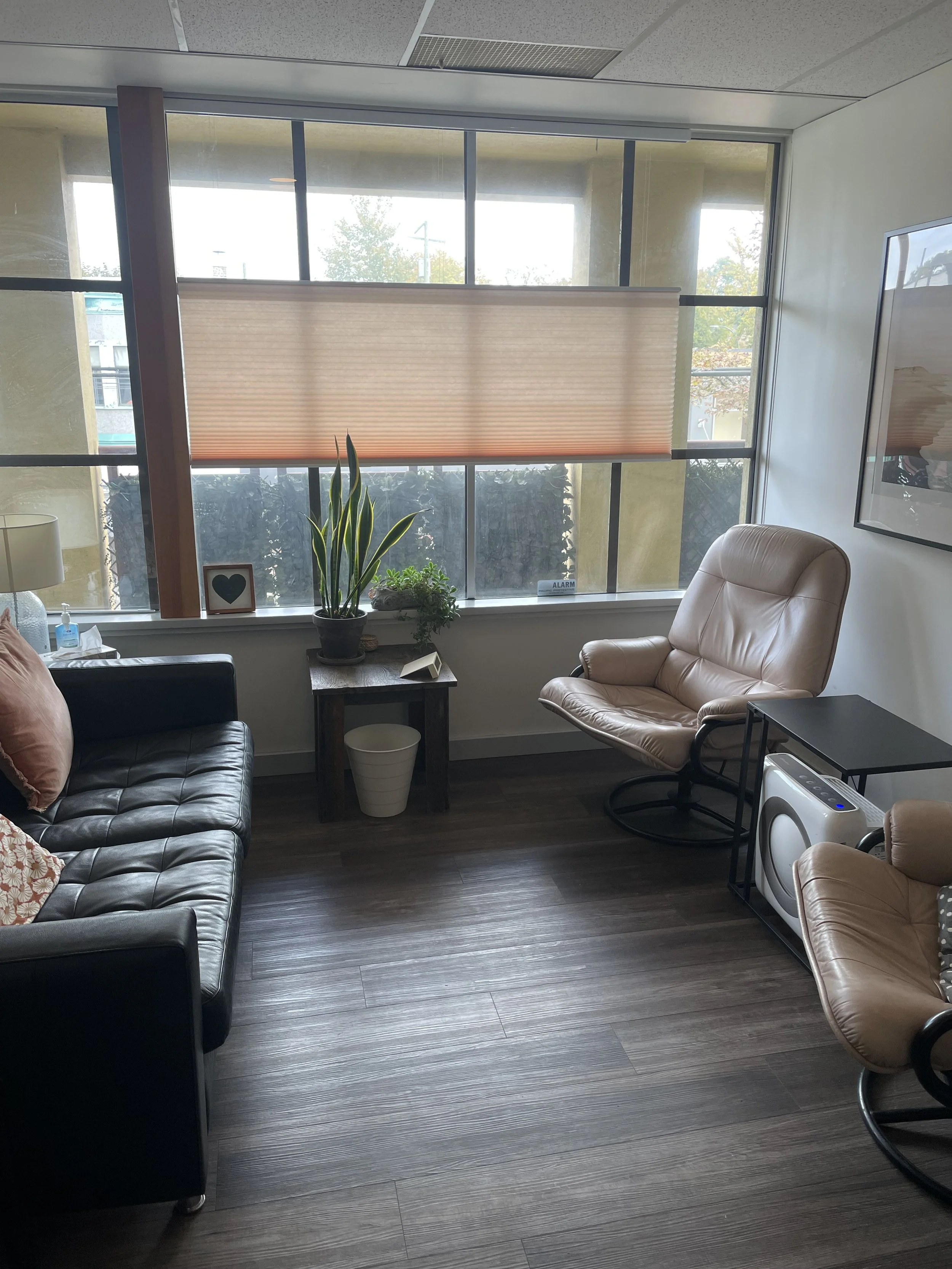 Cozy office corner with a window, two armchairs, a small table with plants, a black leather sofa, and a floor lamp.