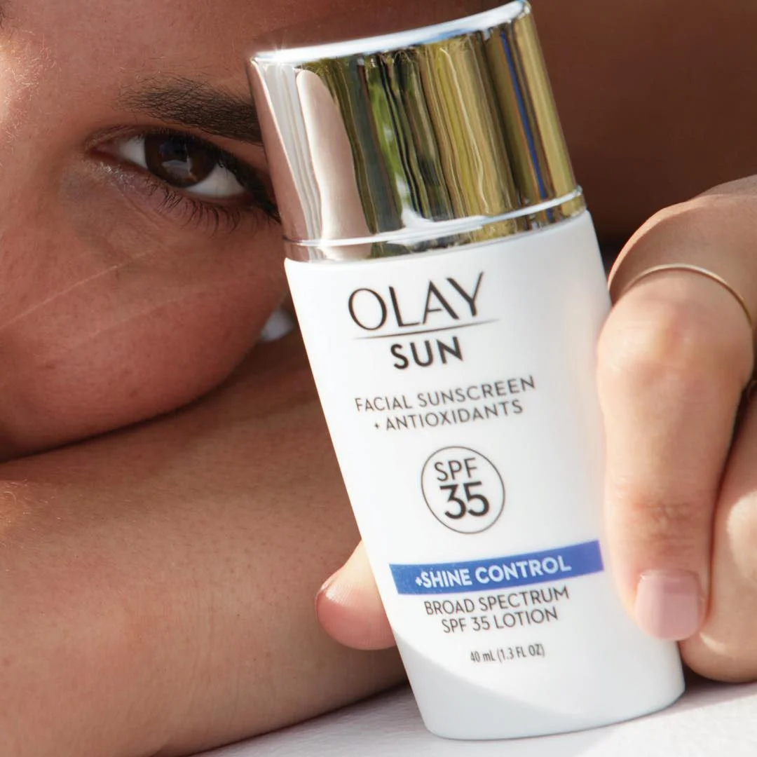 A person holding a bottle of Olay Sun SPF 35 Broad Spectrum Lotion close to their face, with close-up focus on their eye and the product.