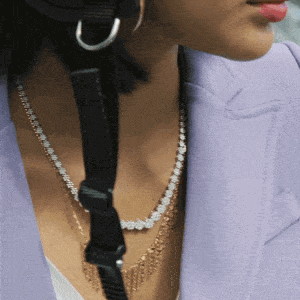 Close-up of a woman wearing layered necklaces, a purple blazer, and hoop earrings.