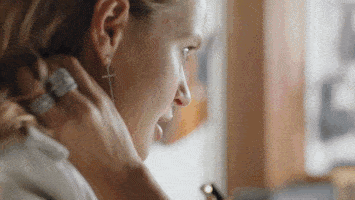 A woman smiling and looking at her phone, with her hand resting on her neck.