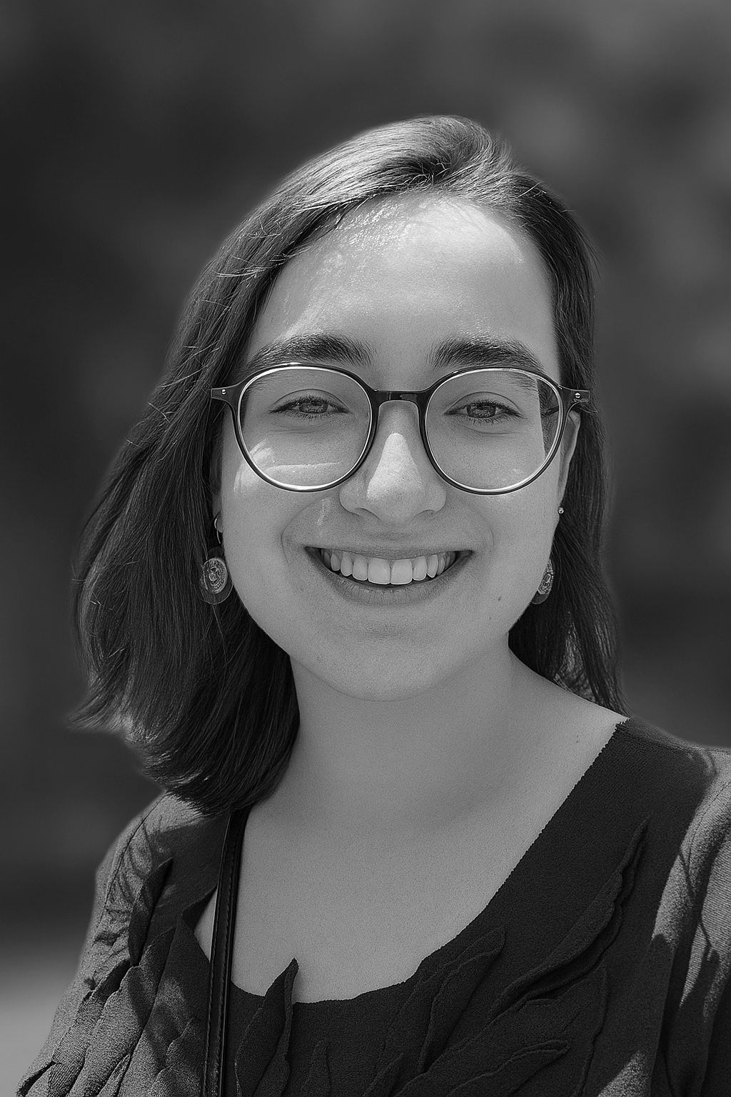 Black and white photo of a woman with shoulder-length hair, glasses, earrings, and a smiling face.
