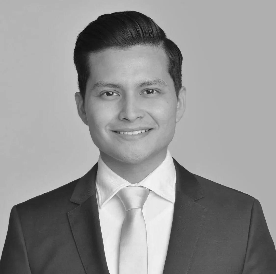 Black and white headshot of a young man in a suit and tie, smiling