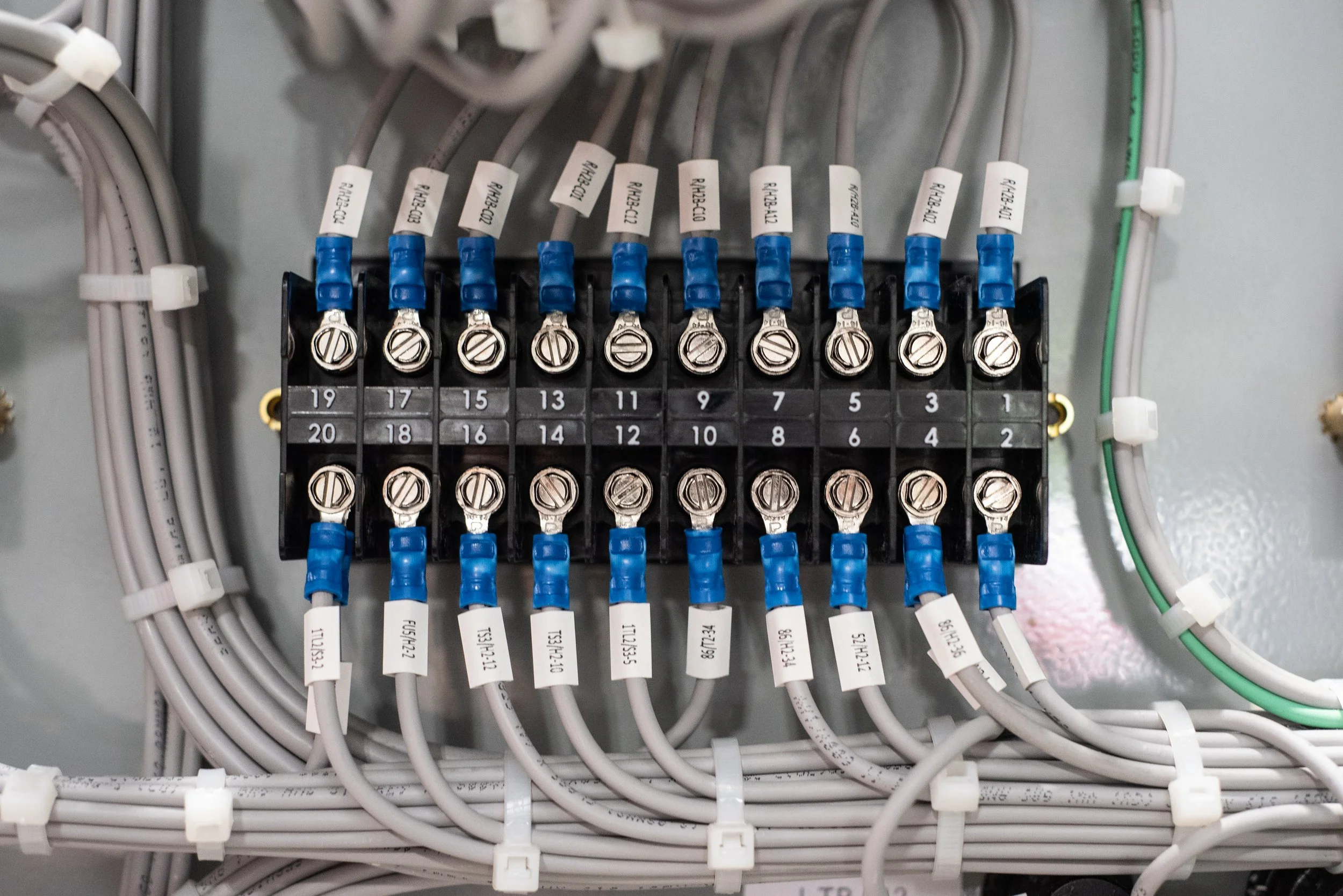 A close-up of an electrical panel with multiple wires connected to terminal blocks, labeled with various codes and numbers, and secured with screws.