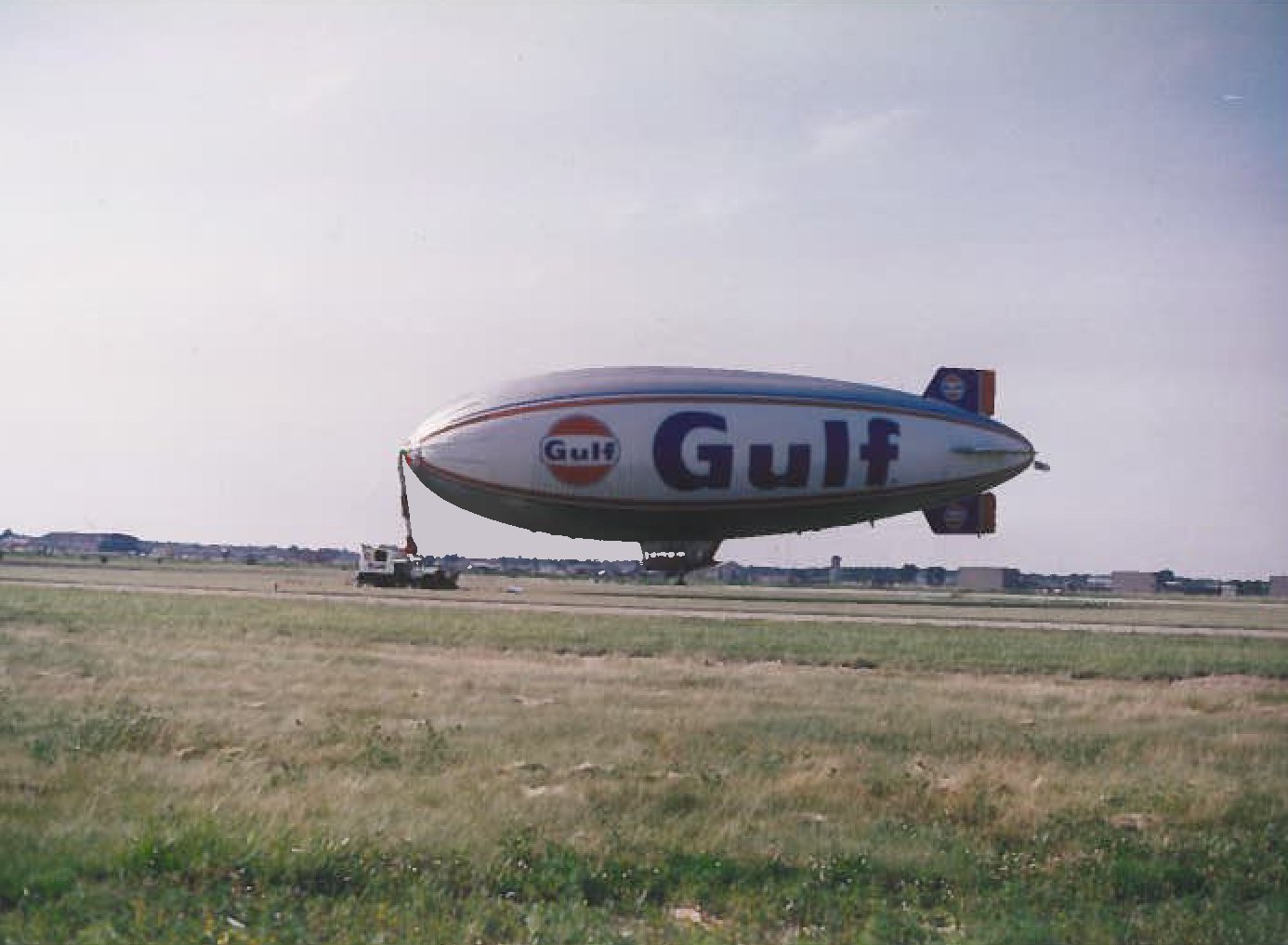A blimp with Gulf branding and logo flying low over an open field.