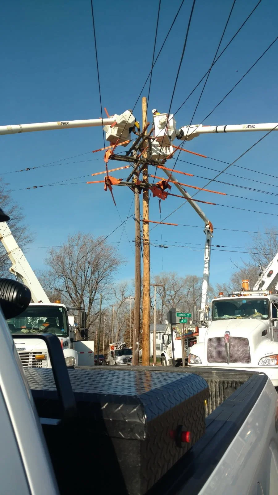 Workers repairing a damaged utility pole with electrical wires, using bucket trucks on a clear day.