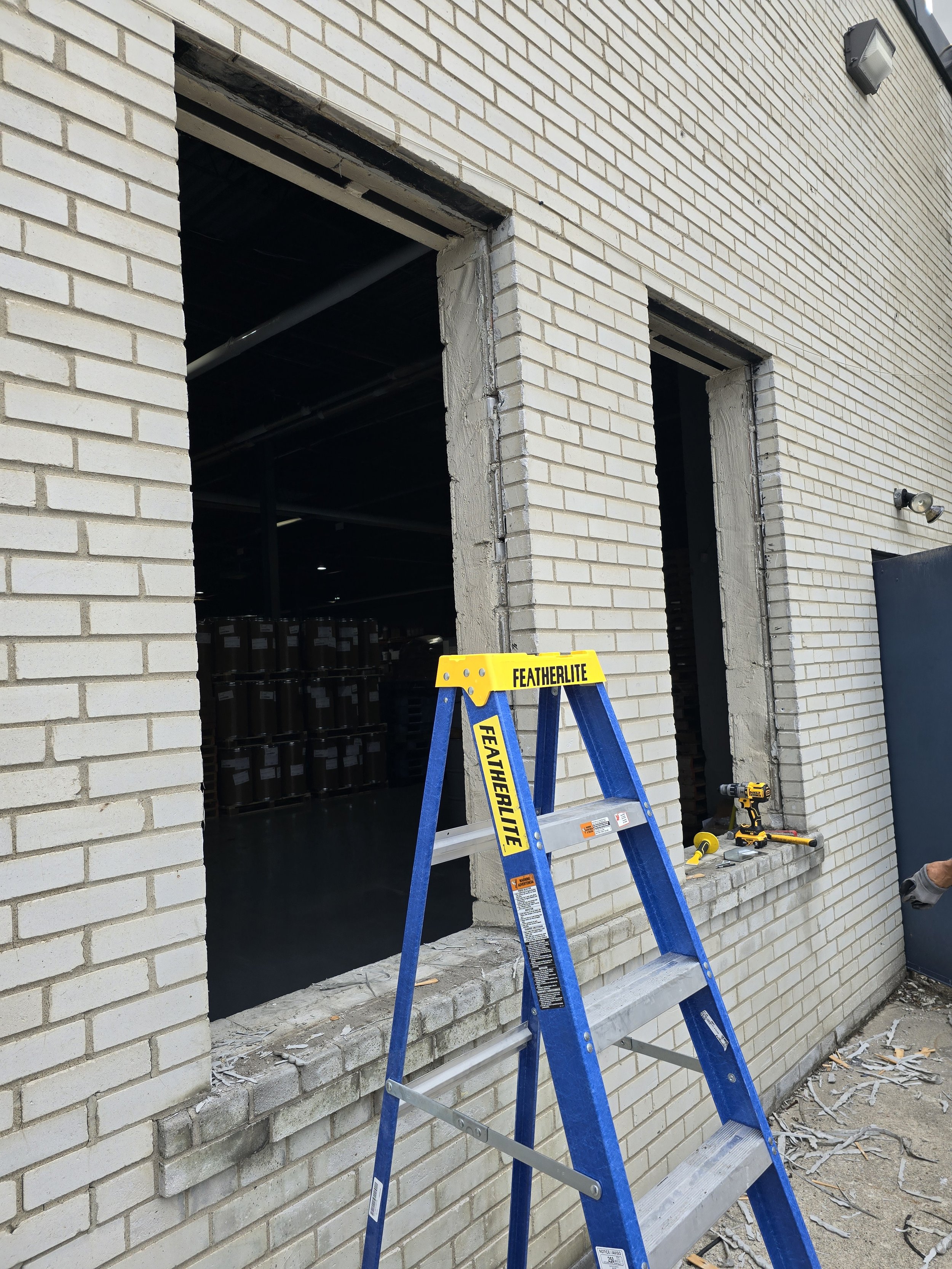 Construction site with a blue ladder and an open window without glass in a brick wall, with tools placed on the windowsill.