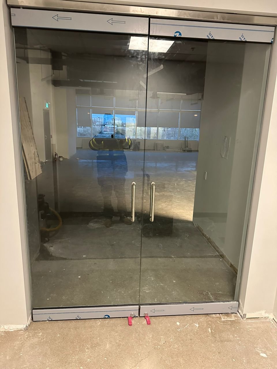 Clear glass double doors with metal handles in an unfinished interior space.