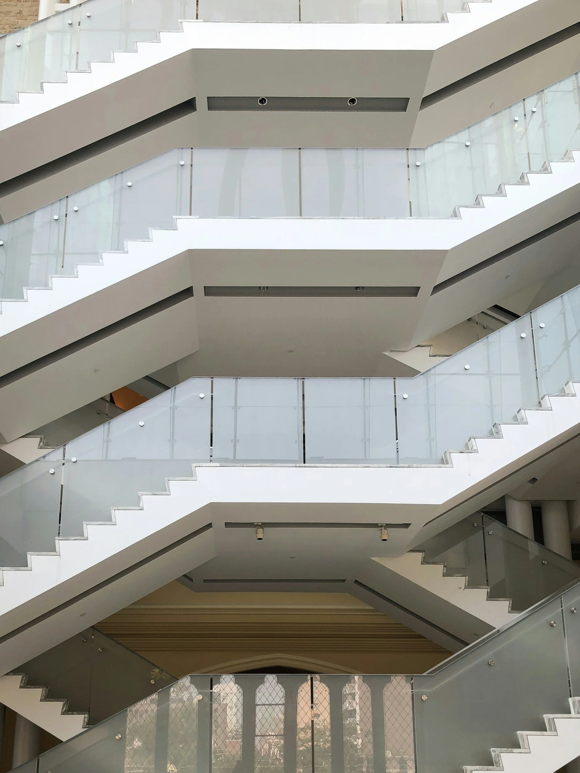 Multiple modern indoor staircases with glass railings and white supports in a building interior.