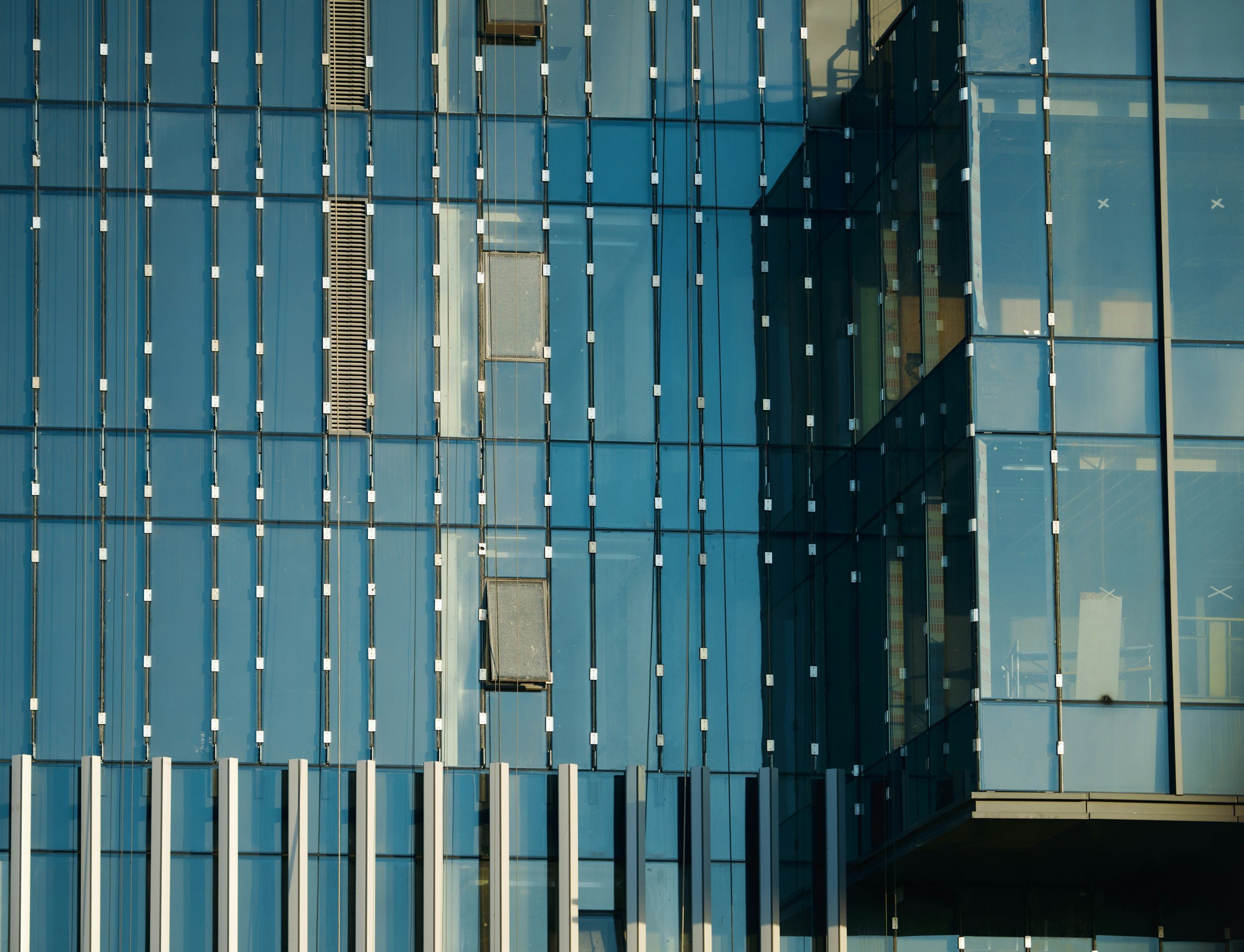 Close-up view of a modern glass building facade with blue-tinted reflective windows and metallic framework.