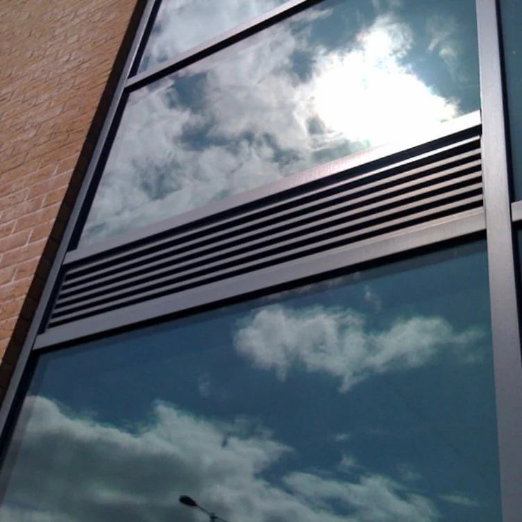 Close-up of a building's exterior window reflecting blue sky and white clouds, with a brick wall on the left.