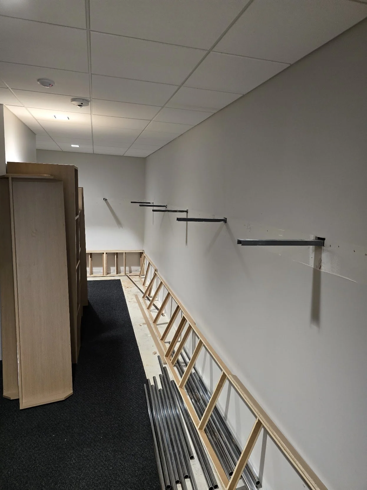 Empty office or retail space under construction with black shelves on the wall and metal tracks on the floor.