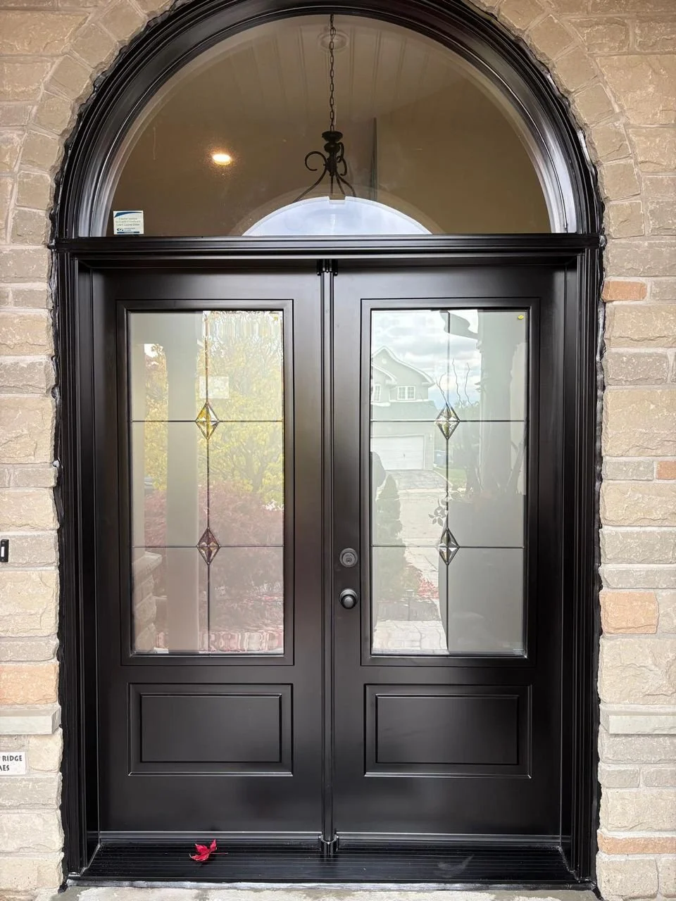 Black double front door with decorative glass panes, arched window above, and brick exterior framing.