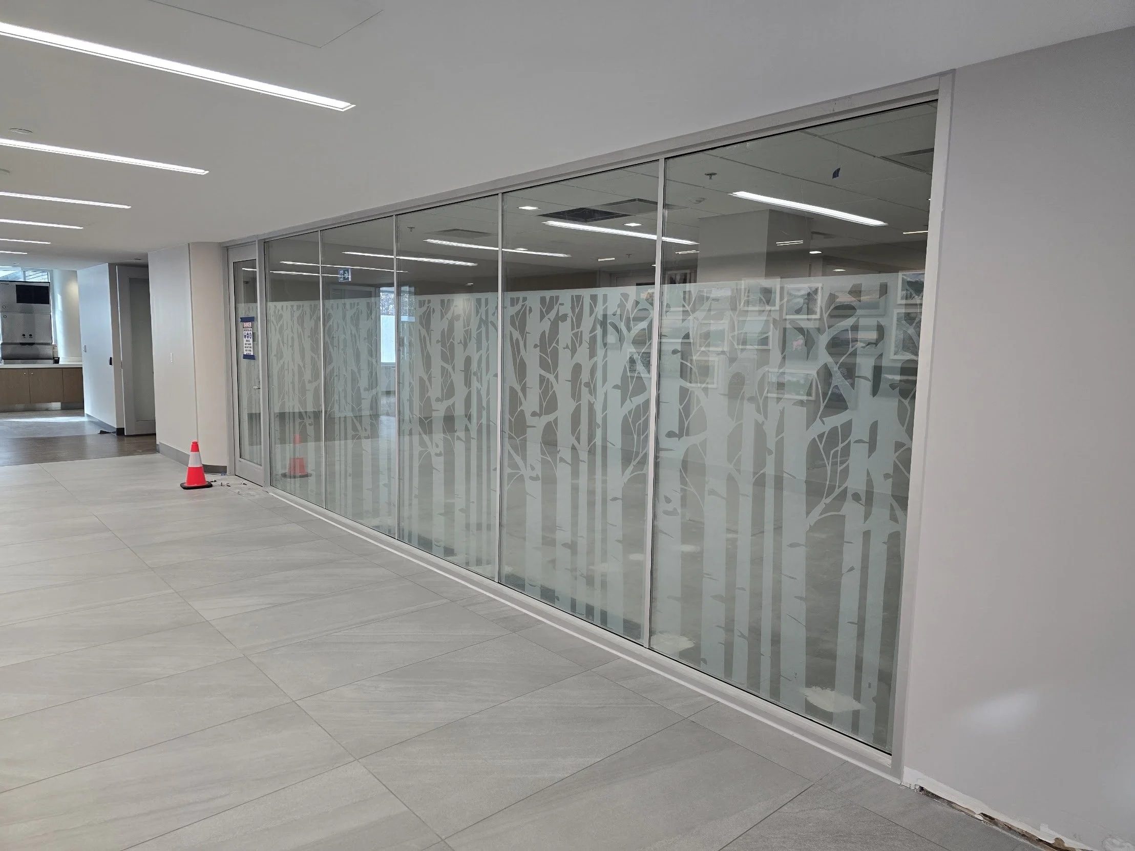Empty office space with glass walls decorated with a tree silhouette pattern, and a red safety cone on the floor.