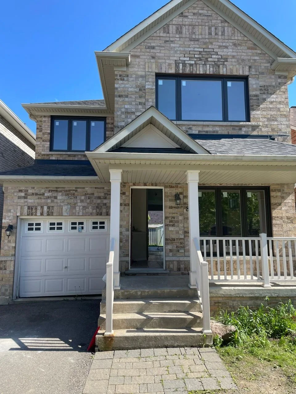 Front view of a two-story house with brick exterior, black-framed windows, a white garage door, and a small covered front porch with stairs and white railing.