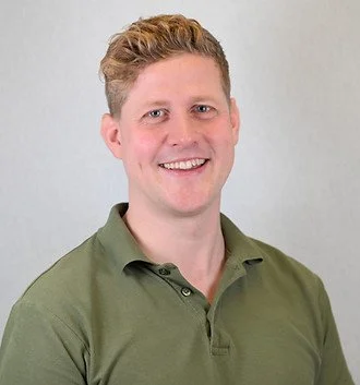 Portræt af en mand med lyst hår og grøn polo shirt, smilende mod kameraet.