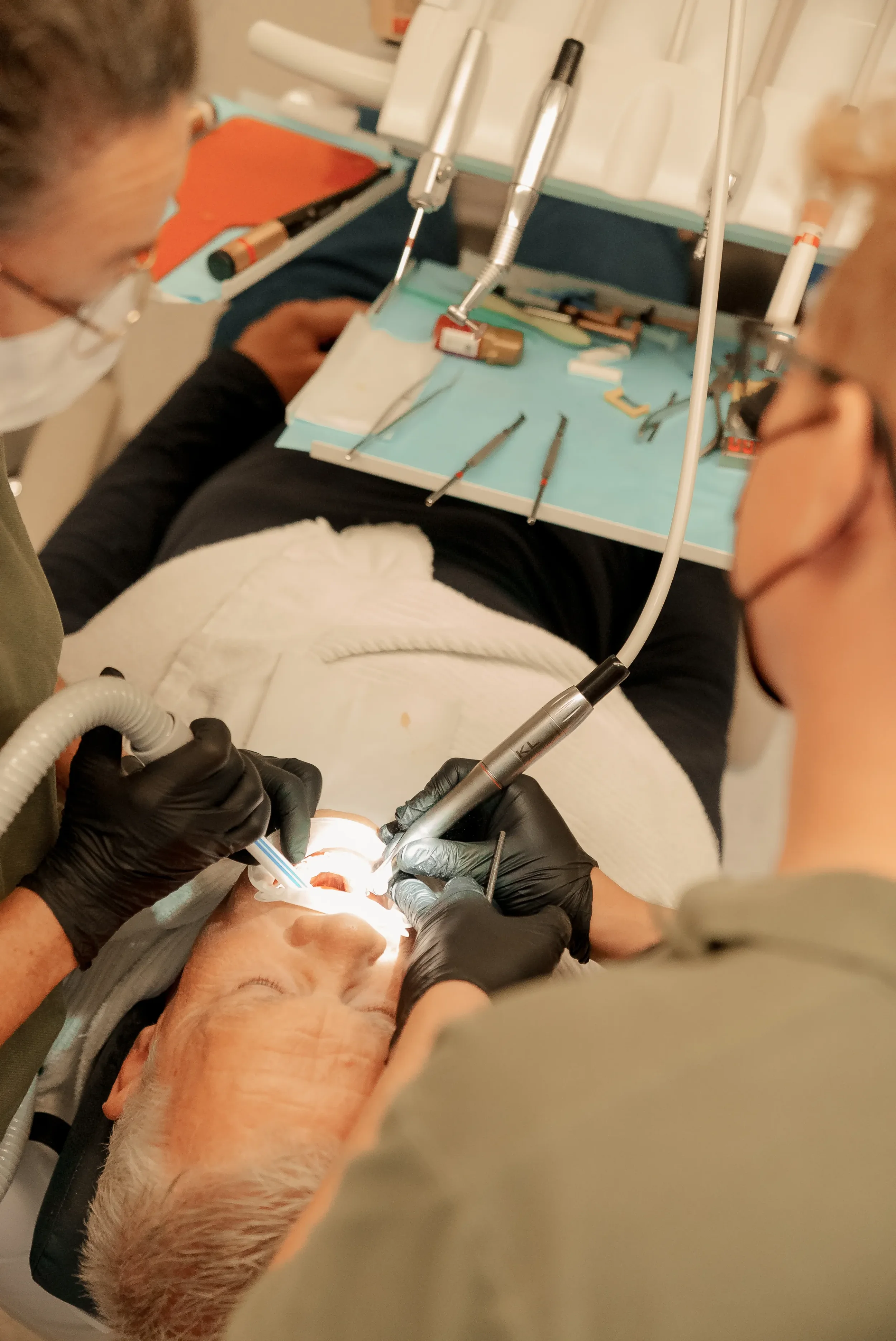 To tandlæger arbejder på en ældre mand, der ligger i en tandlægestol, under en tandbehandling.