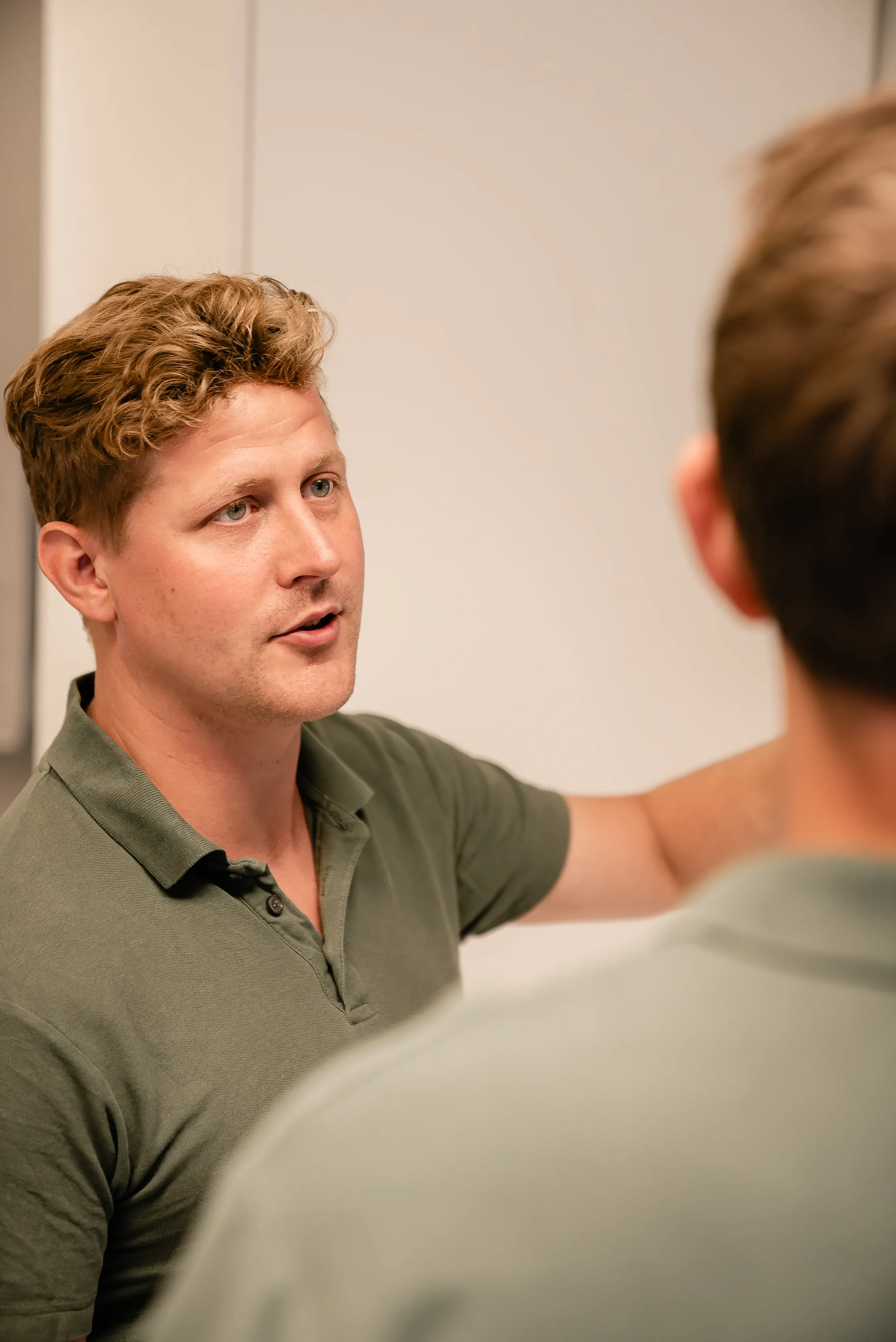 To mænd taler med hinanden, hvor den ene mænd har armen over den andens skulder, i et indendørs miljø.