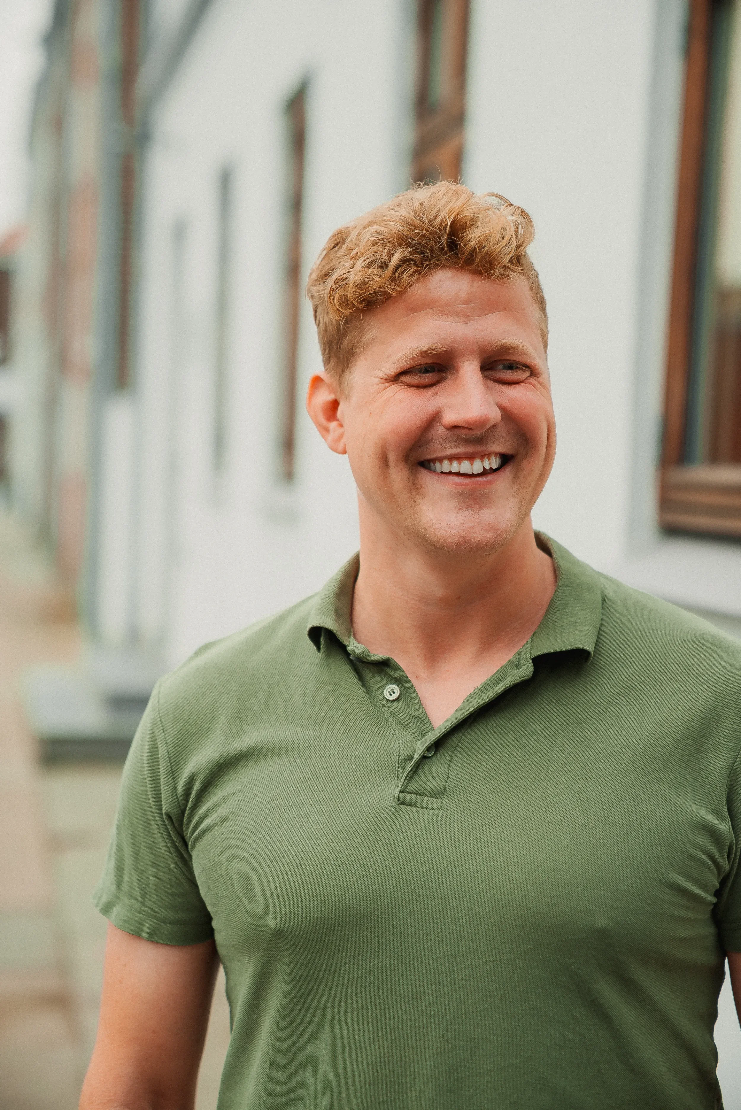 En glad mand med lyst hår, iført en grøn polo-shirt, der smiler udenfor.
