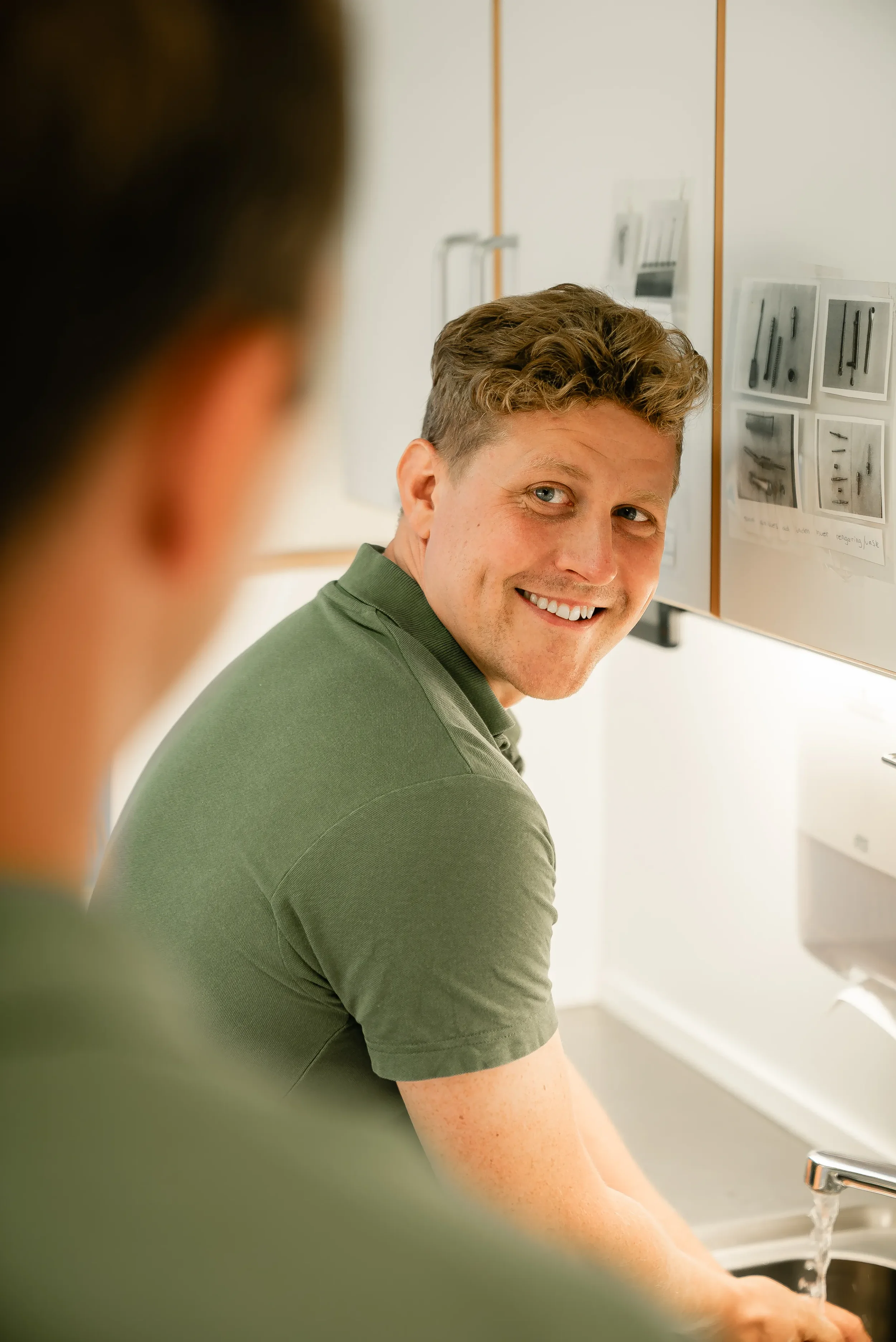 En mand i en grøn polo vasker hænder i en hospitalsvask.