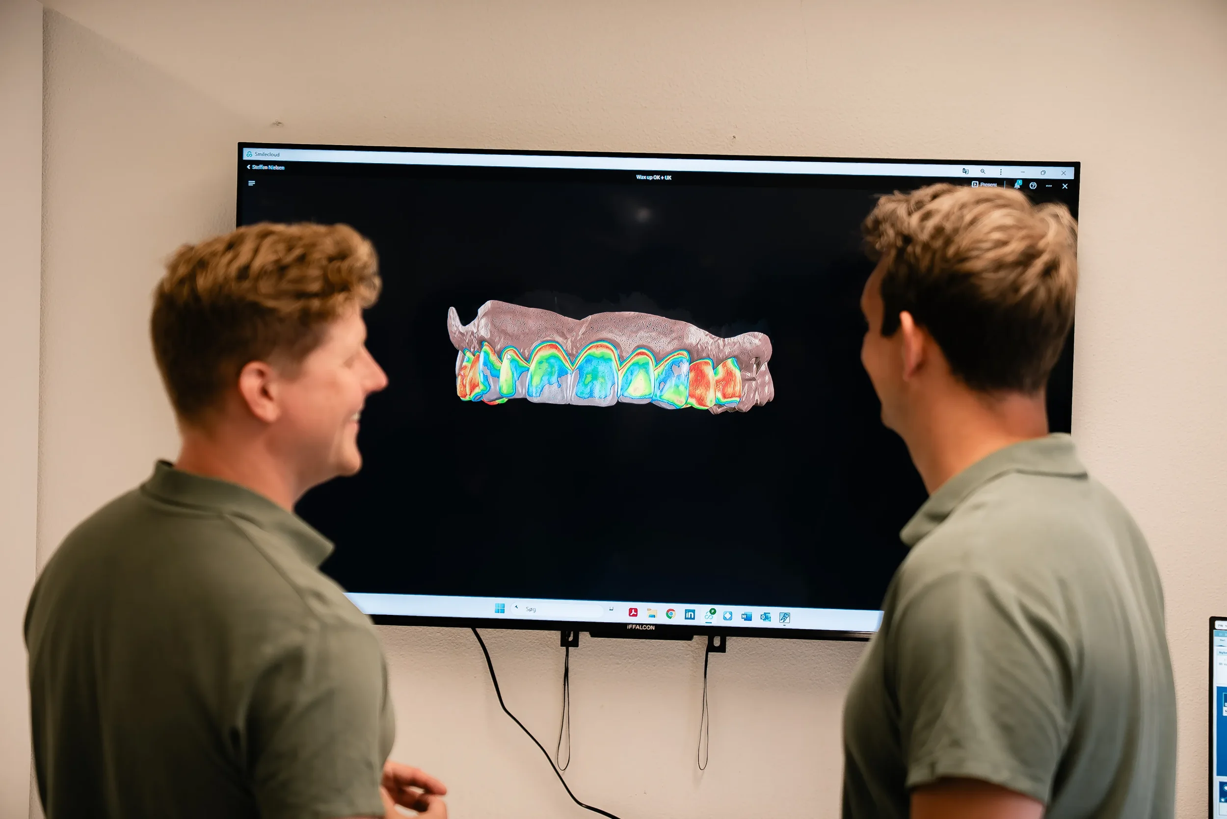 To mænd står foran en computerskærm, der viser en 3D-model af tænder med farverige markeringer.