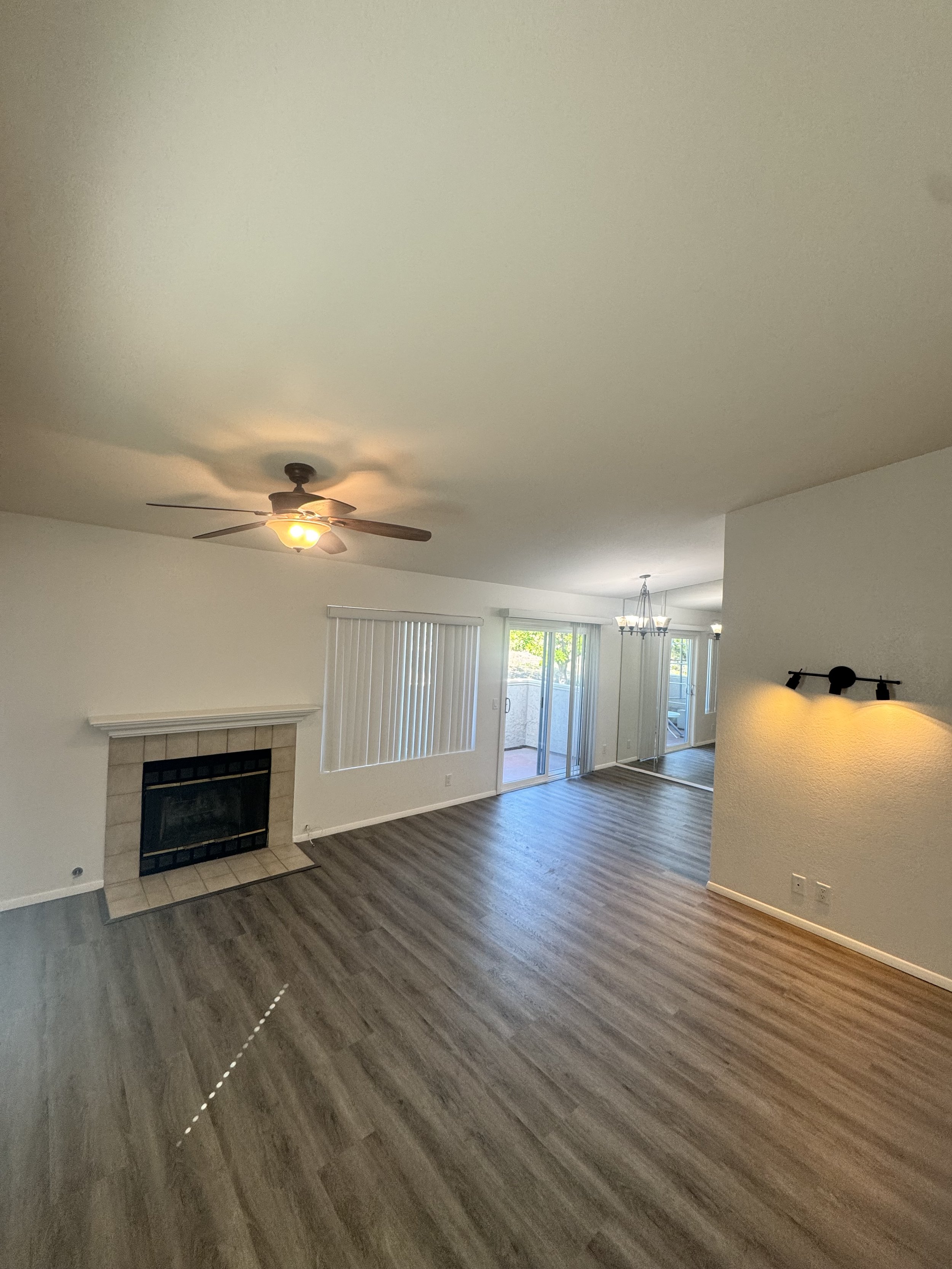 Empty living room with wood-look flooring, a fireplace, sliding glass door leading outside, and ceiling lights.