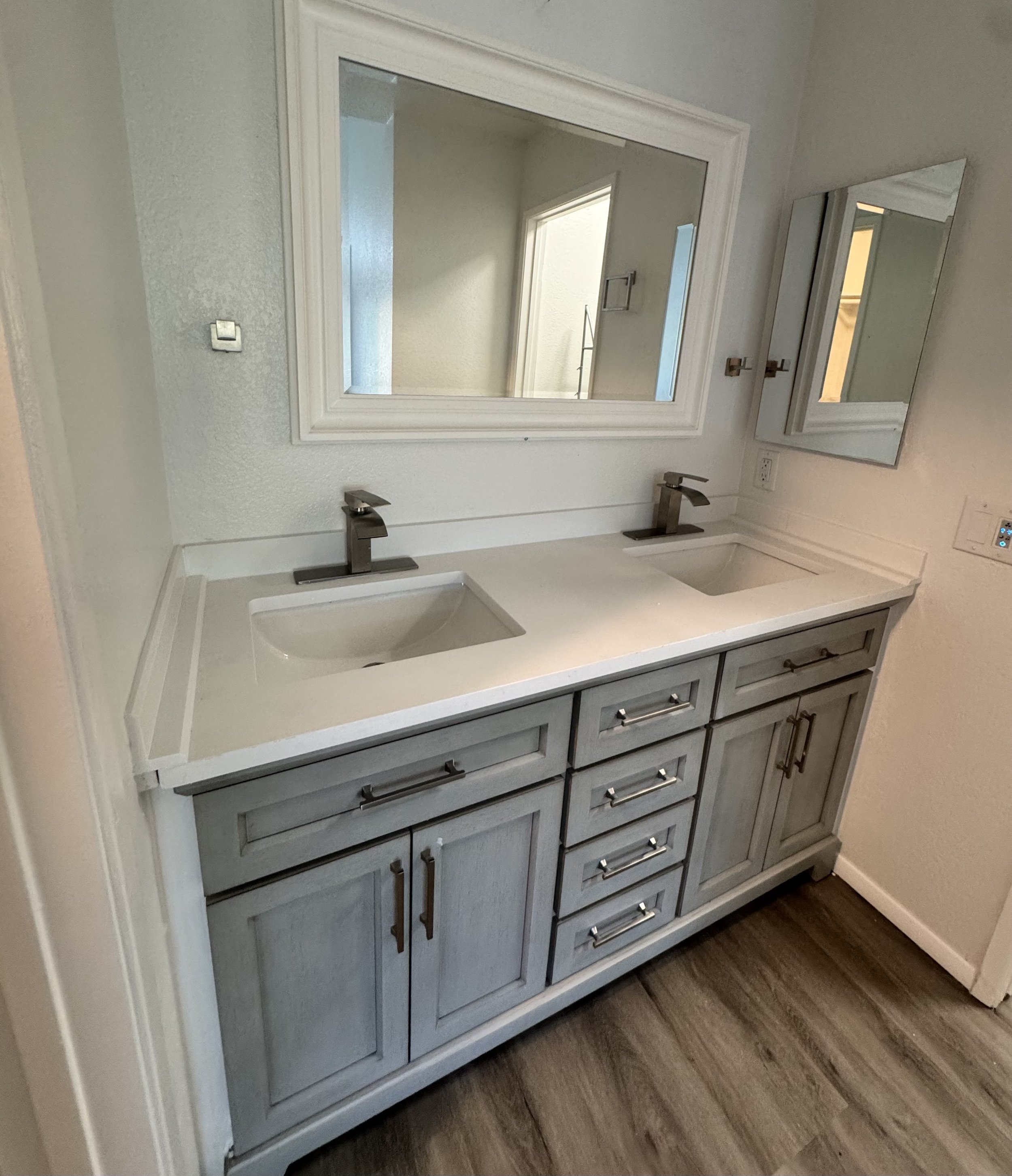 Bathroom vanity with two sinks, large mirror, smaller mirror, and light wood cabinets.