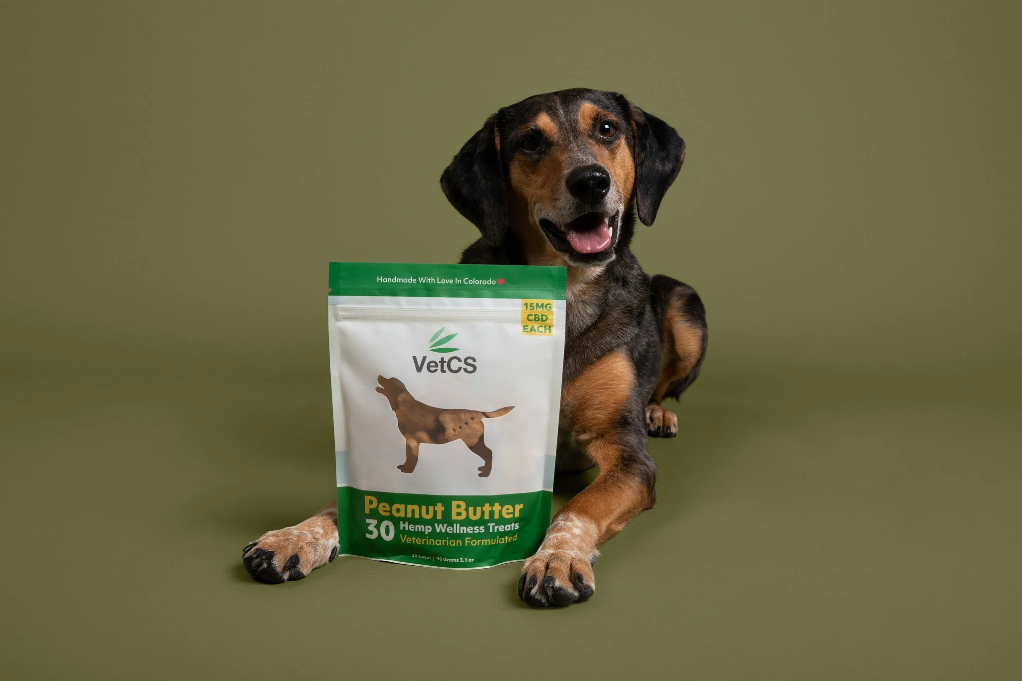 Brown and black dog sitting with a VetCS treats bag