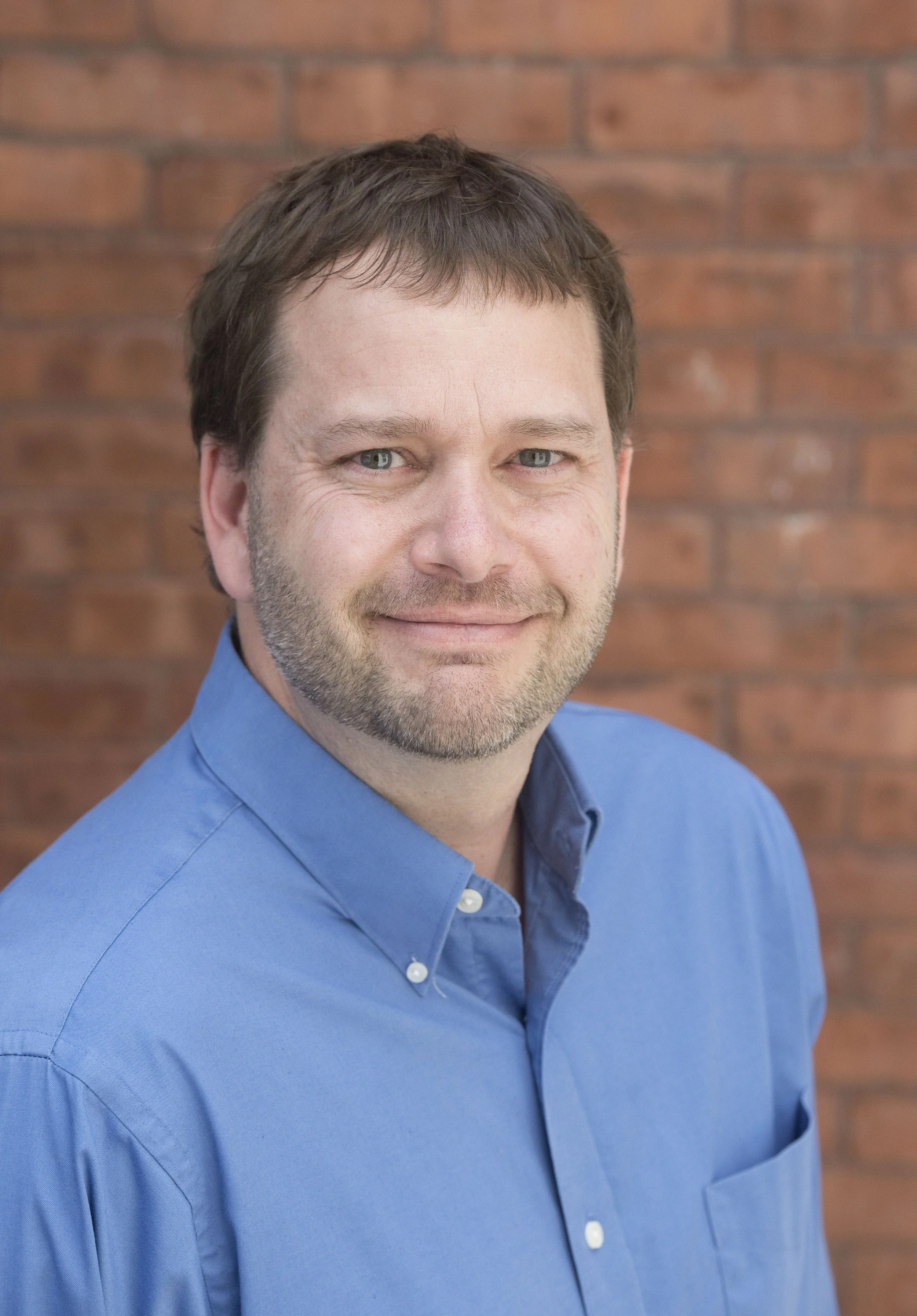 a man in a blue shirt in front of a brick wall