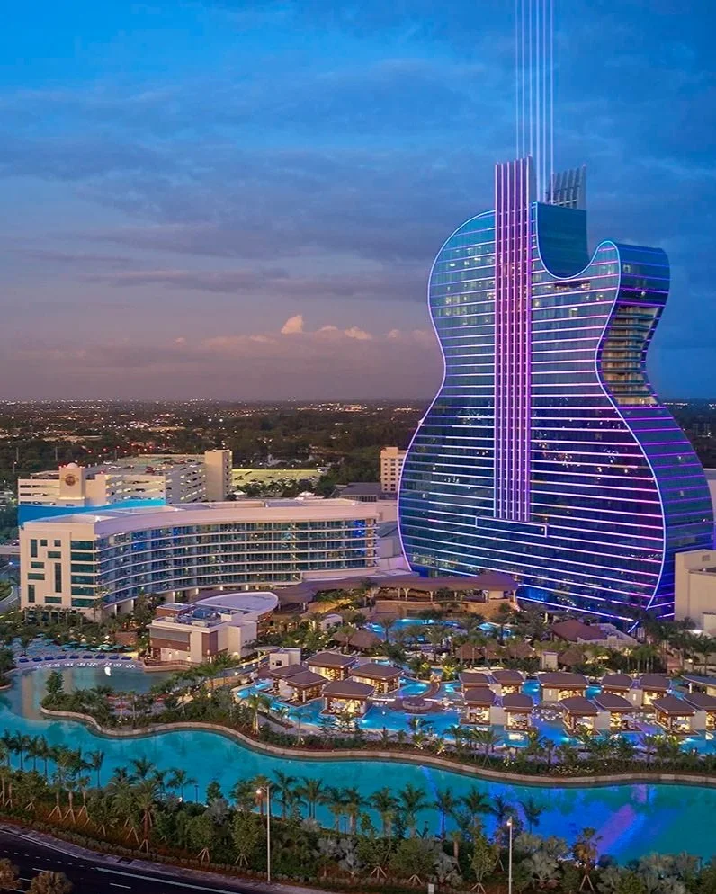 Exterior of a modern black building with an open sliding door revealing an interior art display, surrounded by trees and green grass.