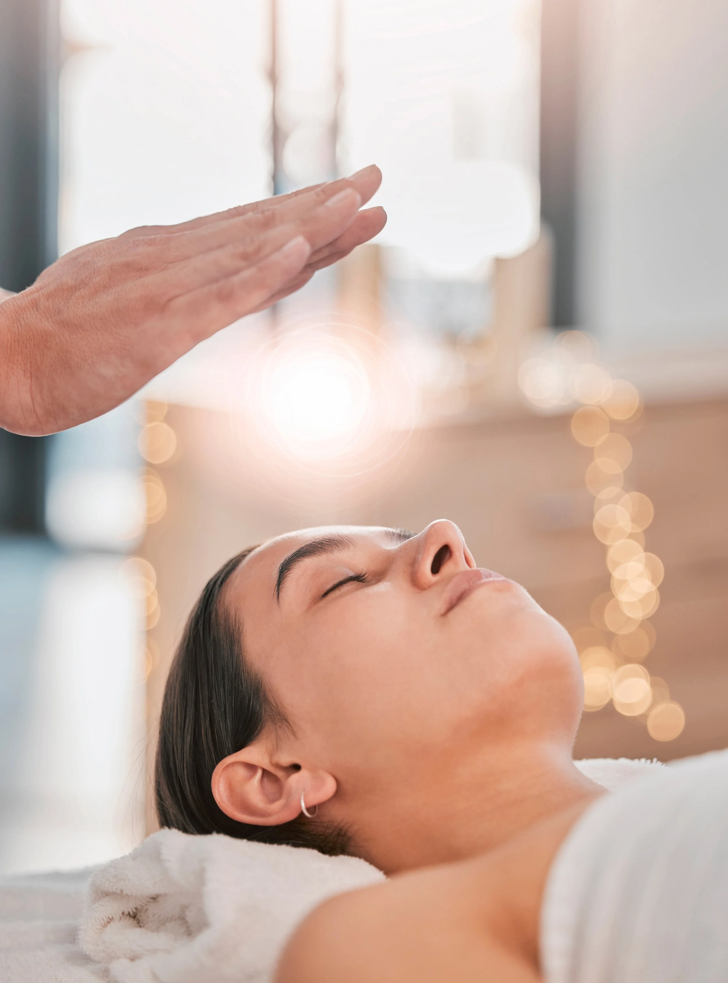 A person receiving reiki healing or energy treatment, lying down with eyes closed, while a hand hovers above them with fingers close together.