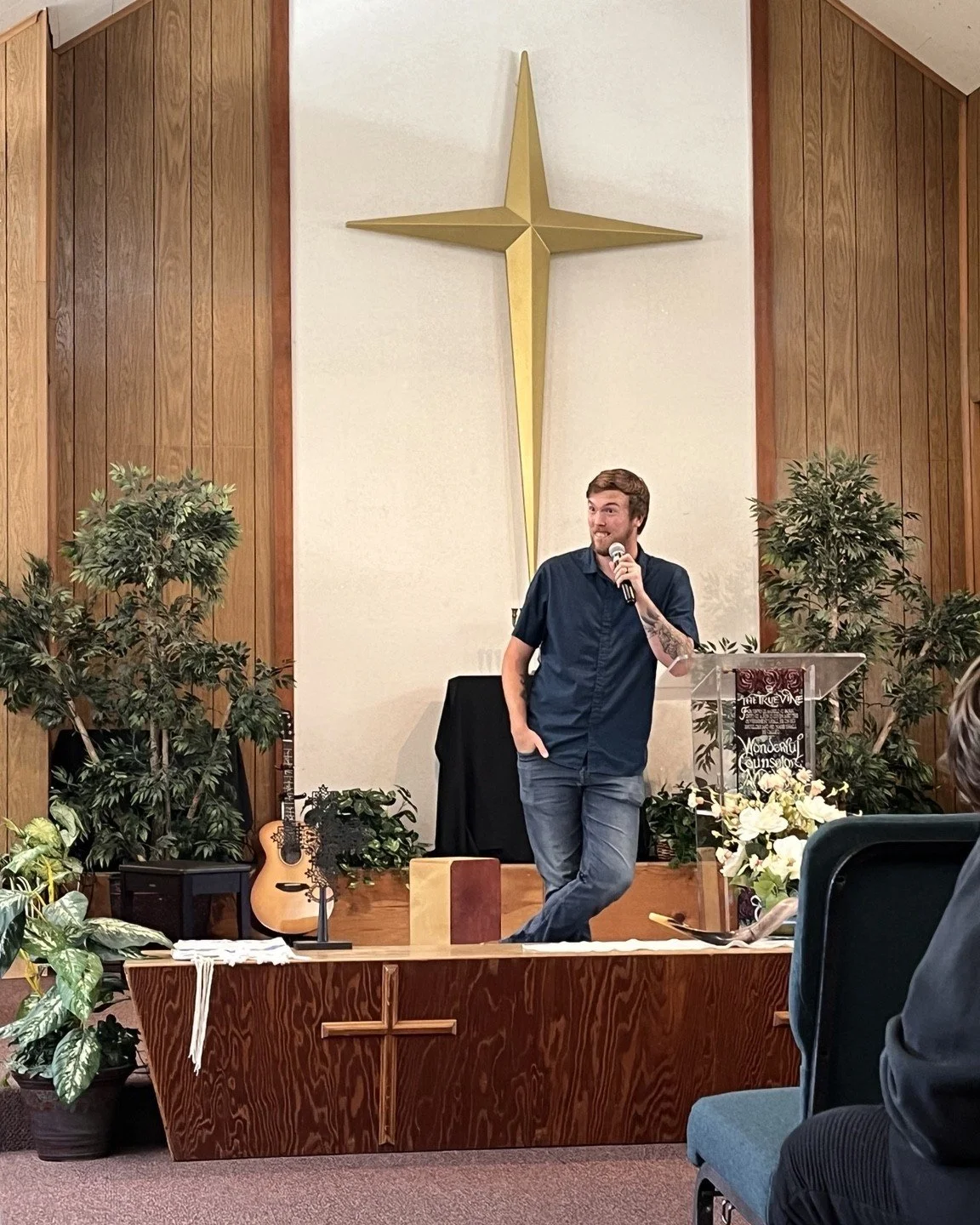 Jeremy Groves preaching beneath a cross at a church gathering.