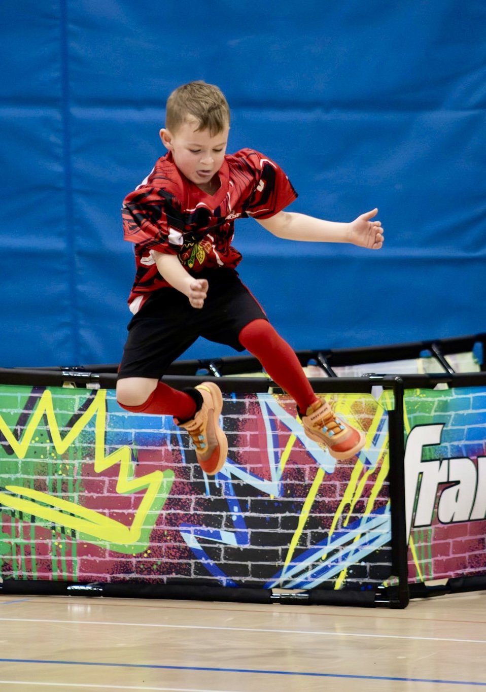 Young athlete leaps over a rink board during an indoor Sunday Funday Sports game near Downers Grove IL