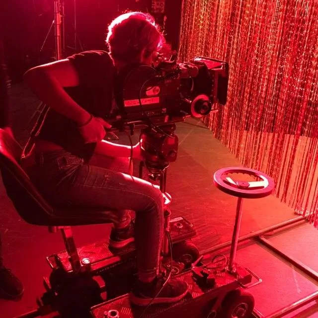 Miriam Ouchi operating a 16mm camera mounted on a moving platform in a red-lit studio
