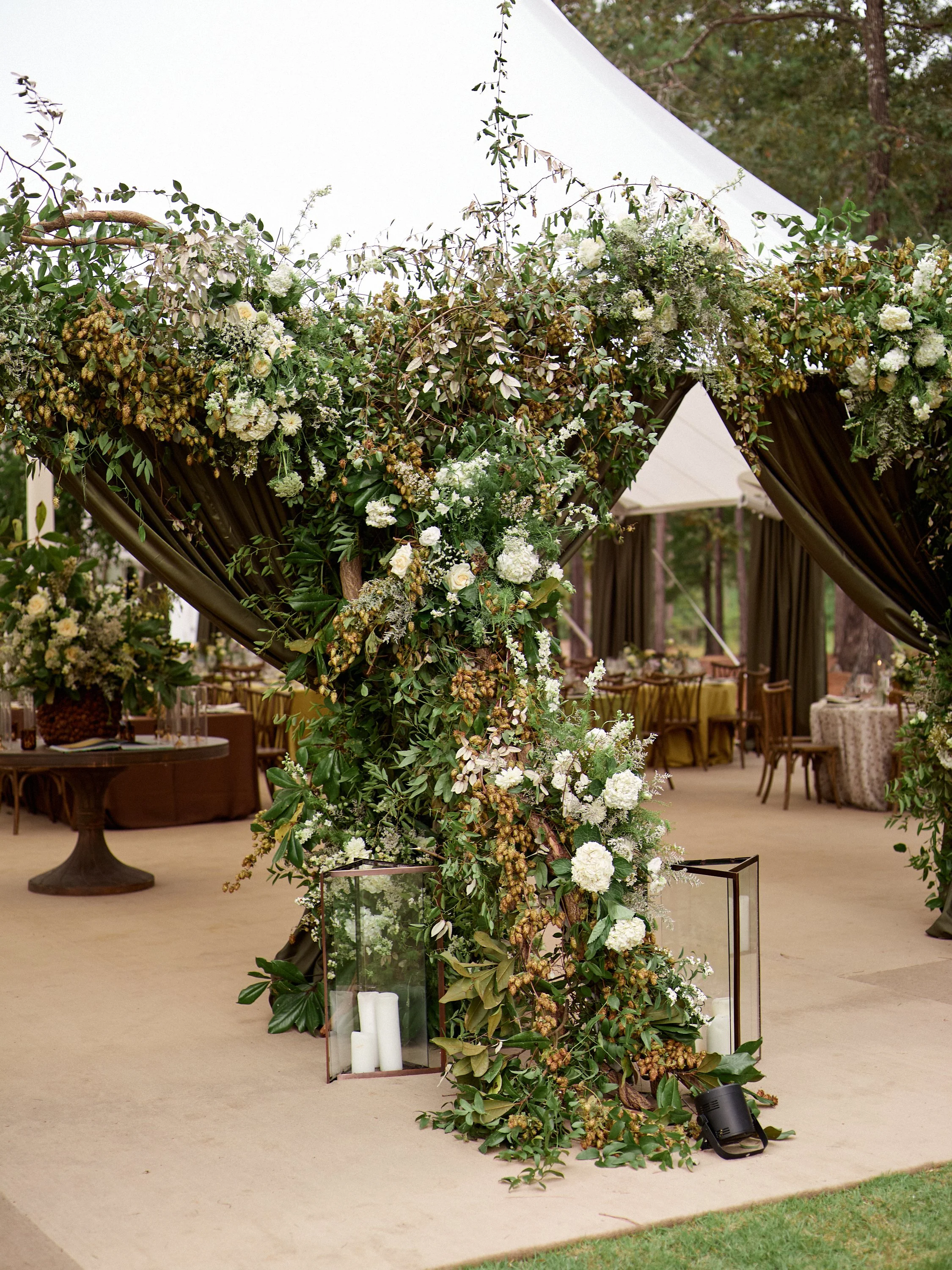 Decorated wedding arch with white flowers and greenery under a white tent