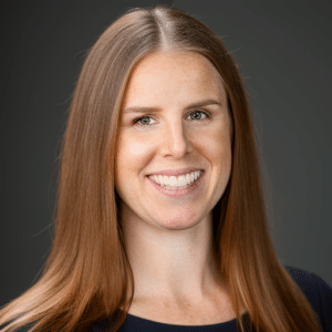 A smiling middle-aged man with glasses and gray hair standing outdoors near a modern building with curved architecture.