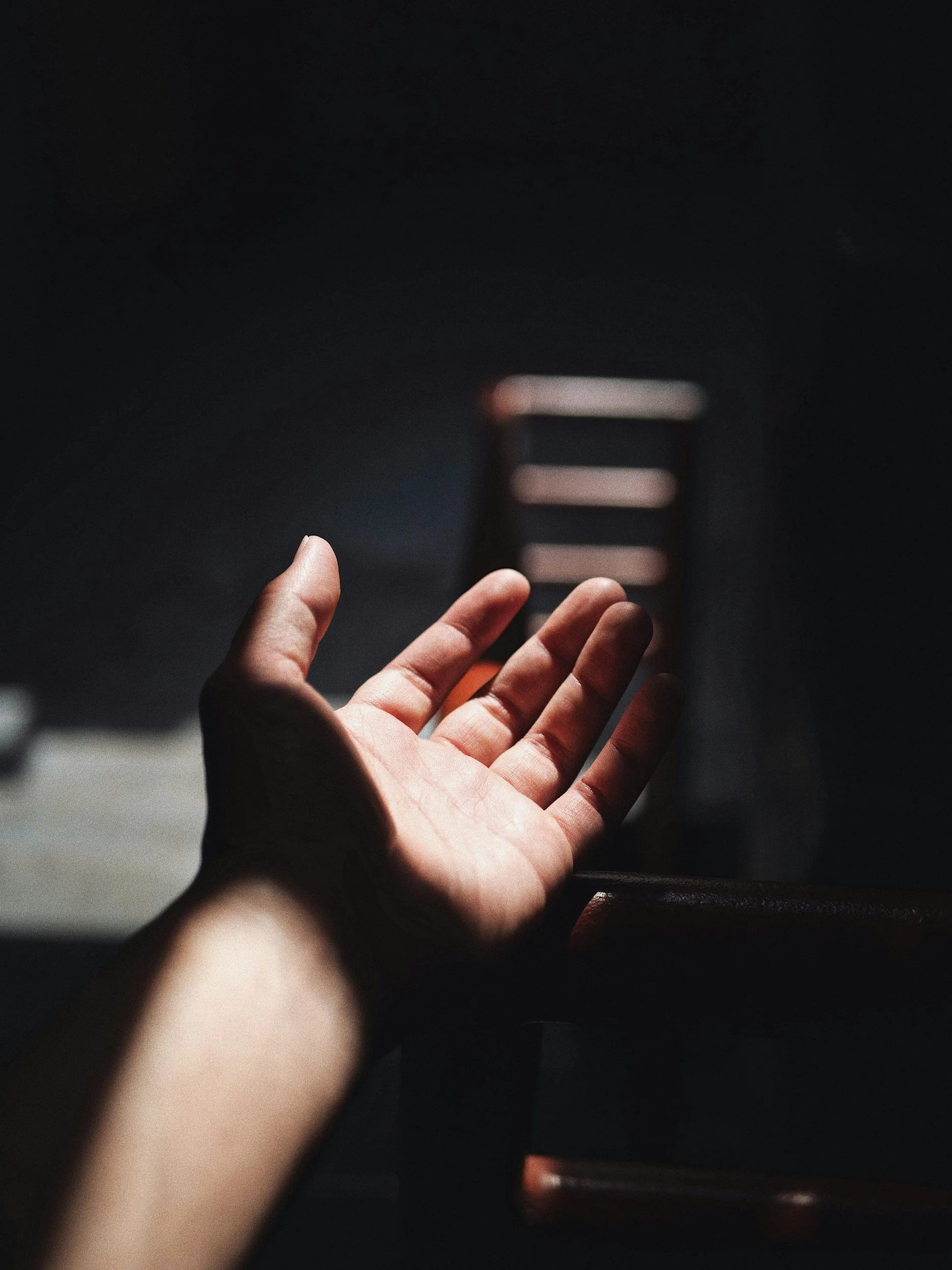 A hand reaching out towards a staircase in a dark environment with minimal lighting.