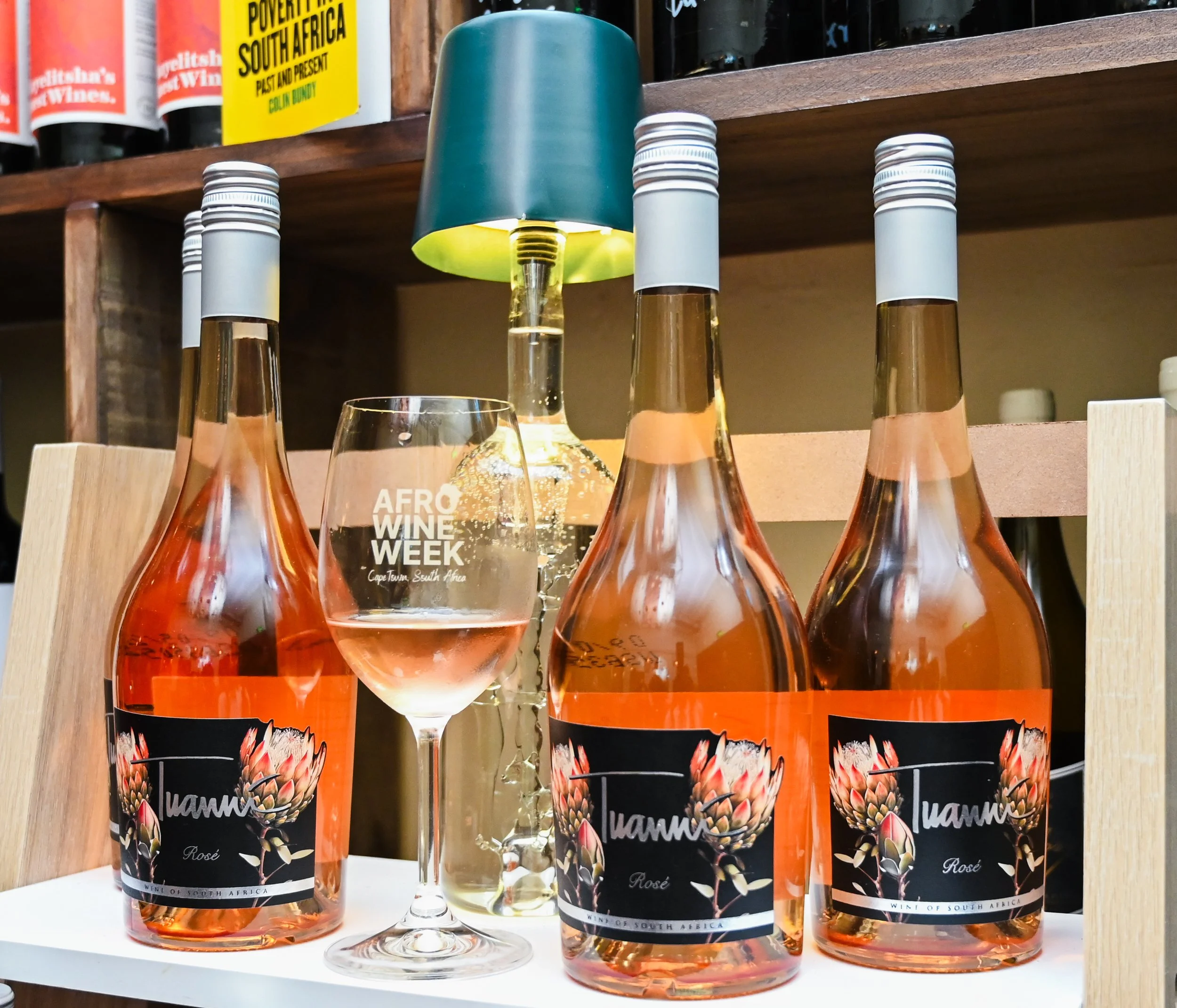 A glass of red wine on a balcony railing with a vineyard, lake, and mountains in the background.
