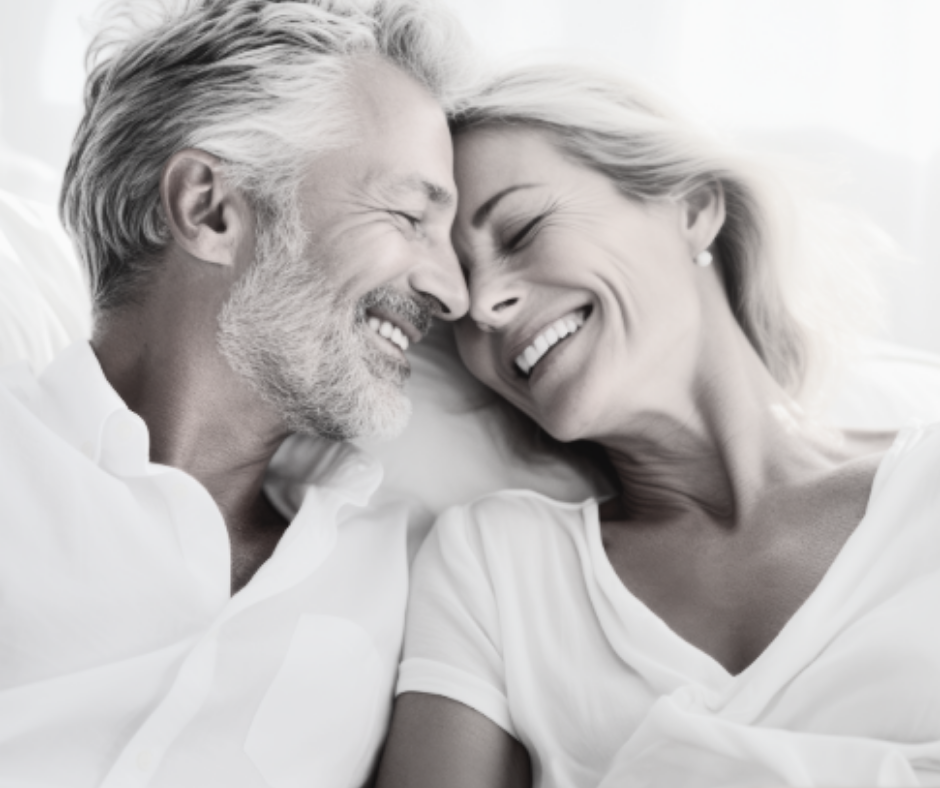 A happy middle-aged man and woman with gray hair lying close together with their foreheads touching, smiling and enjoying each other's company.