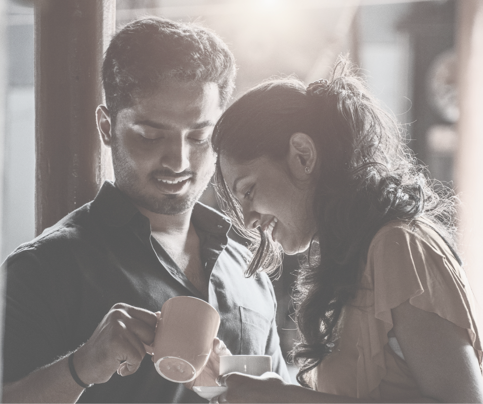 A young man and woman smiling and enjoying coffee together near a window, with sunlight coming in.